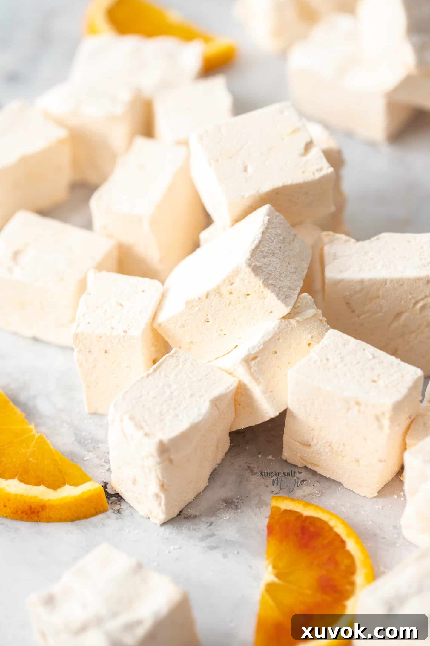A beautifully composed pile of homemade orange marshmallows, each perfectly cut and dusted, resting on a sophisticated grey marble surface. This image evokes the joy of gifting homemade treats.