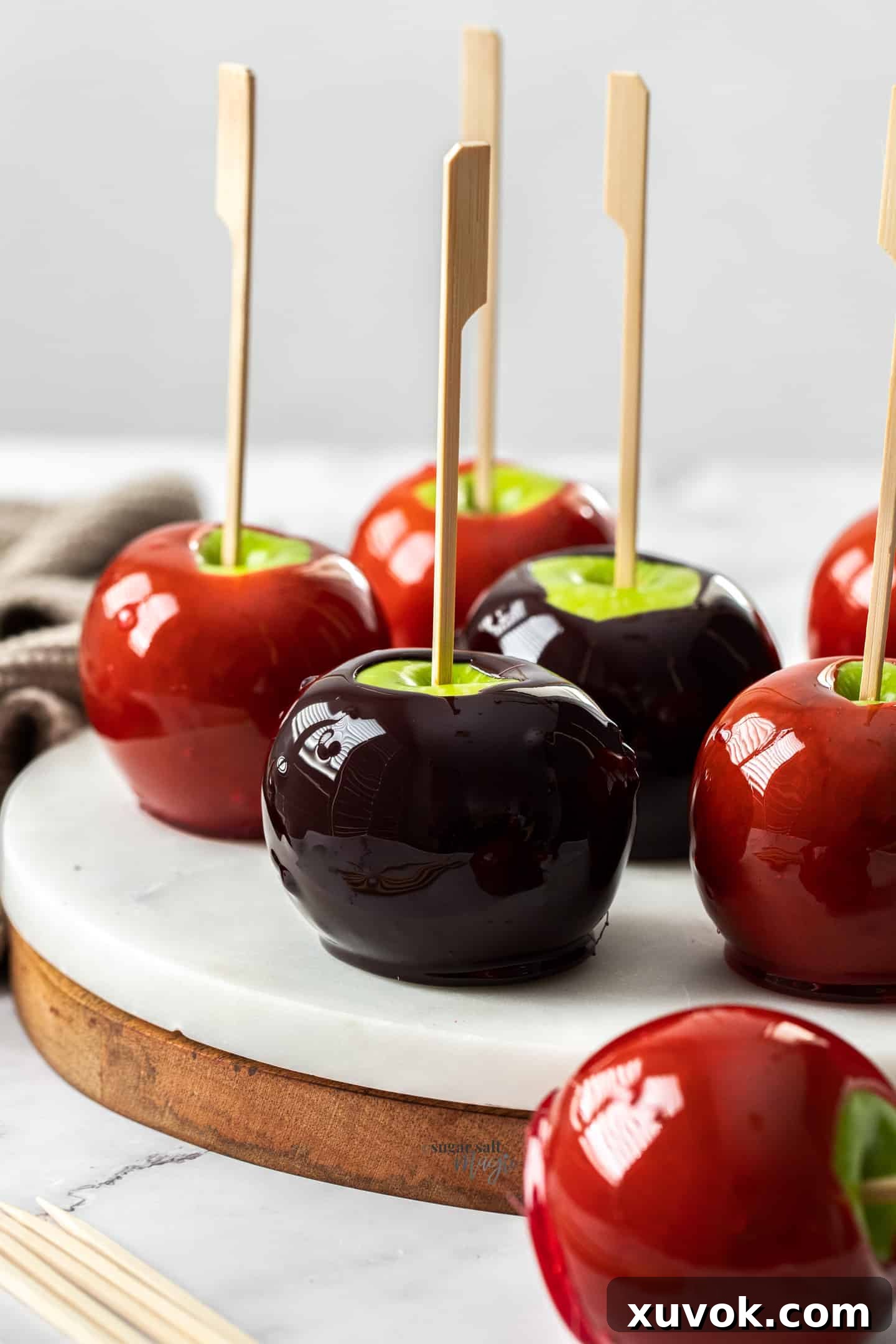 Red and black toffee apples on a white marble platter.