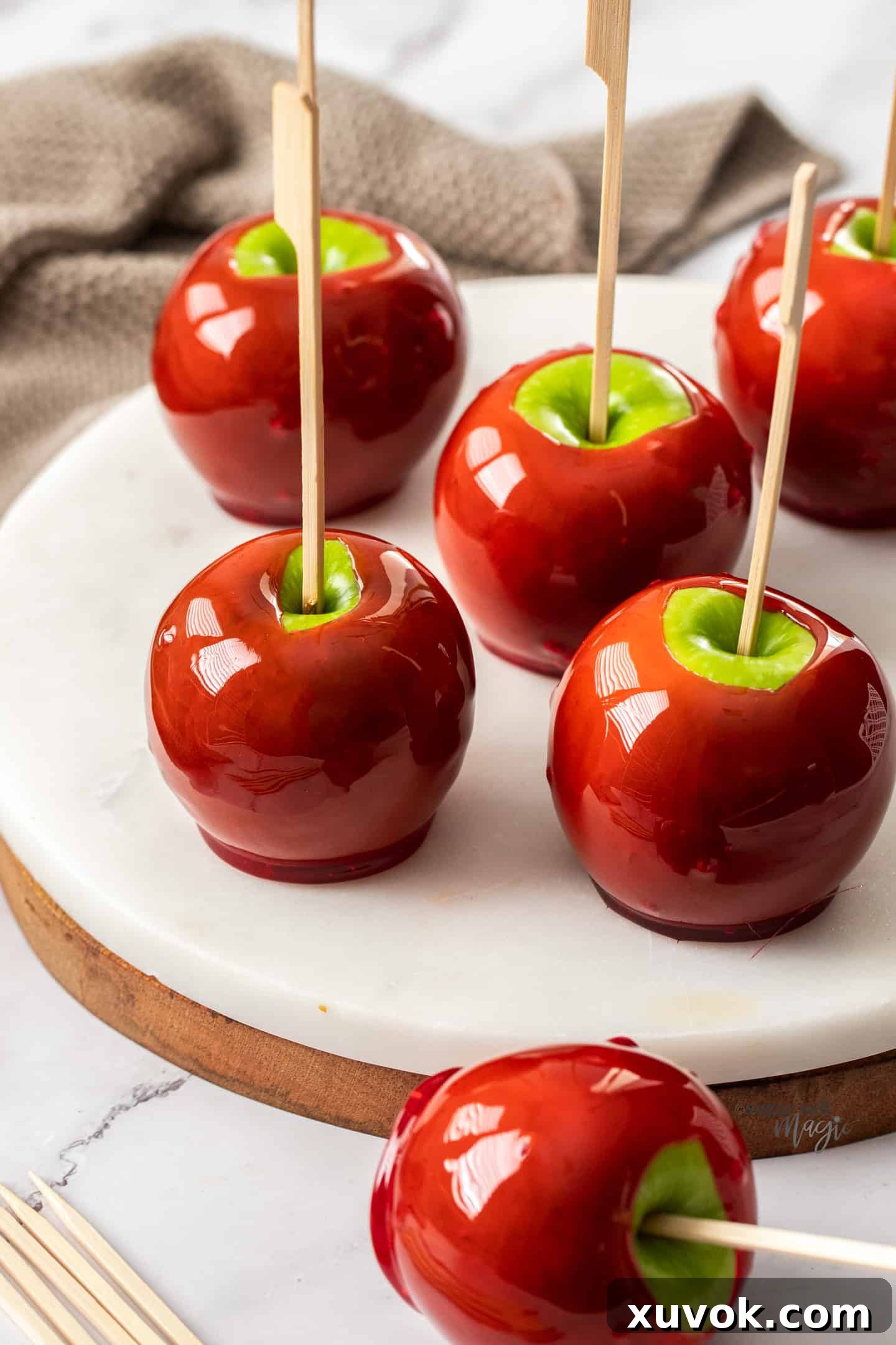 6 red toffee apples on a white marble platter.