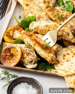 A serving fork digging into some chicken pieces on a tray, showcasing the juicy and tender texture of Greek seasoned chicken, ready to be enjoyed.