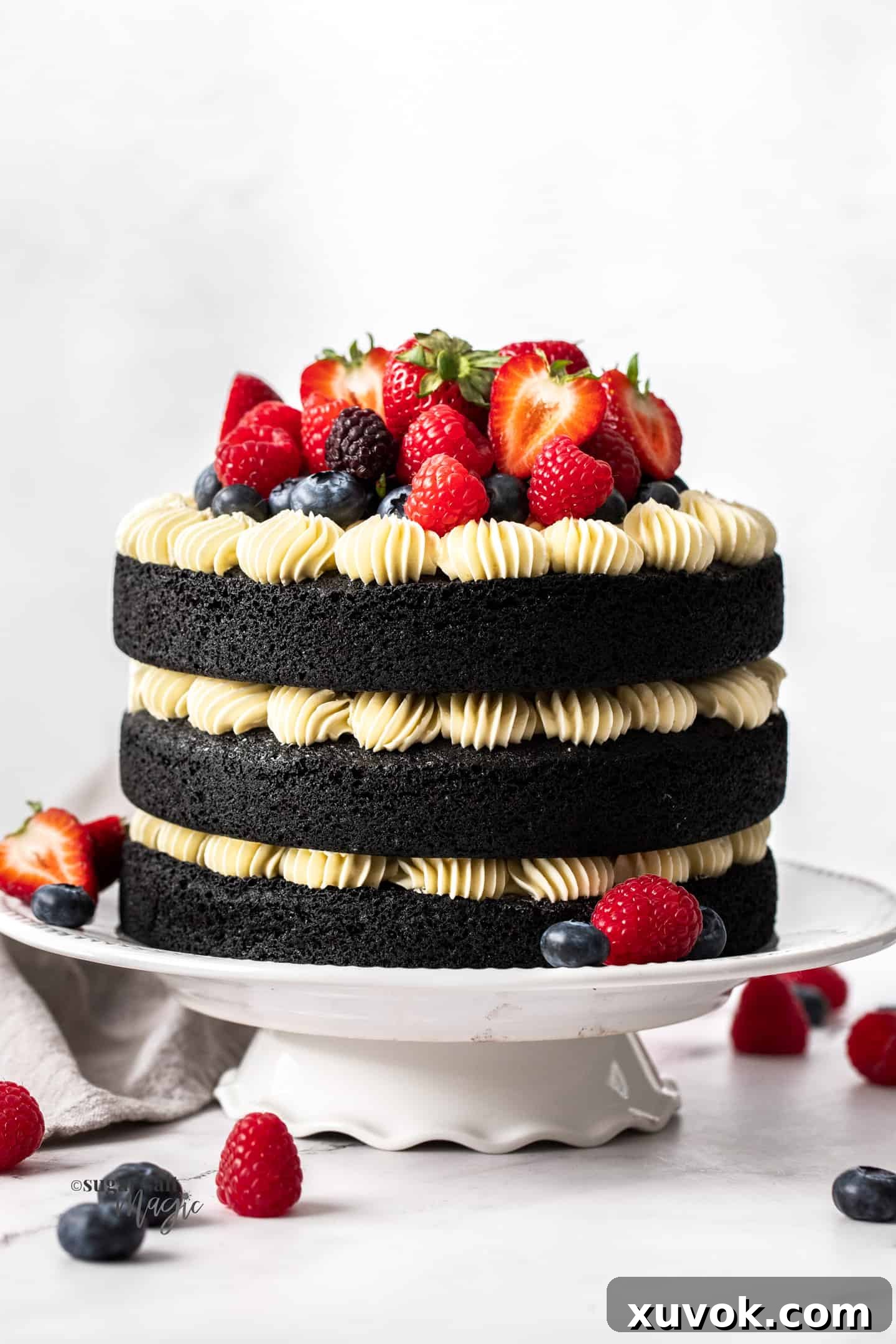 Front on view of a 3 tier black velvet cake topped with fresh berries, showcasing its dramatic dark color and elegant frosting.