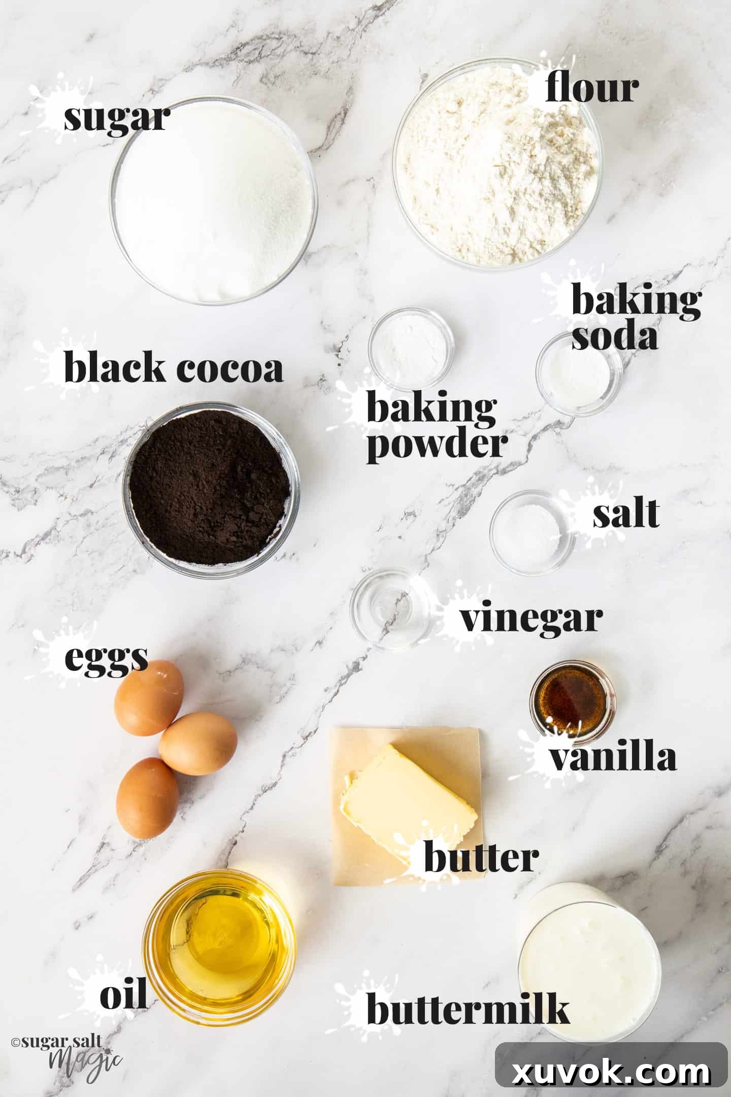 A flat lay image displaying all the individual ingredients for black velvet cake on a elegant marble surface.