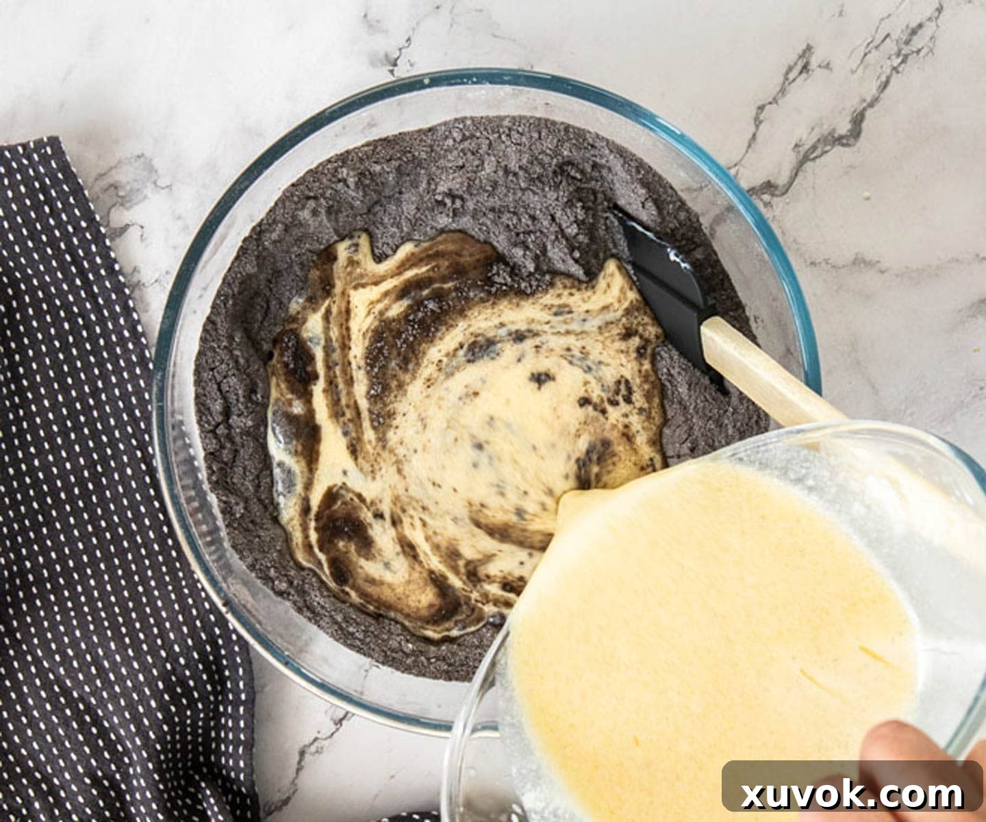 Wet ingredients being carefully added to a well created in the dry ingredients mixture in a large glass bowl.