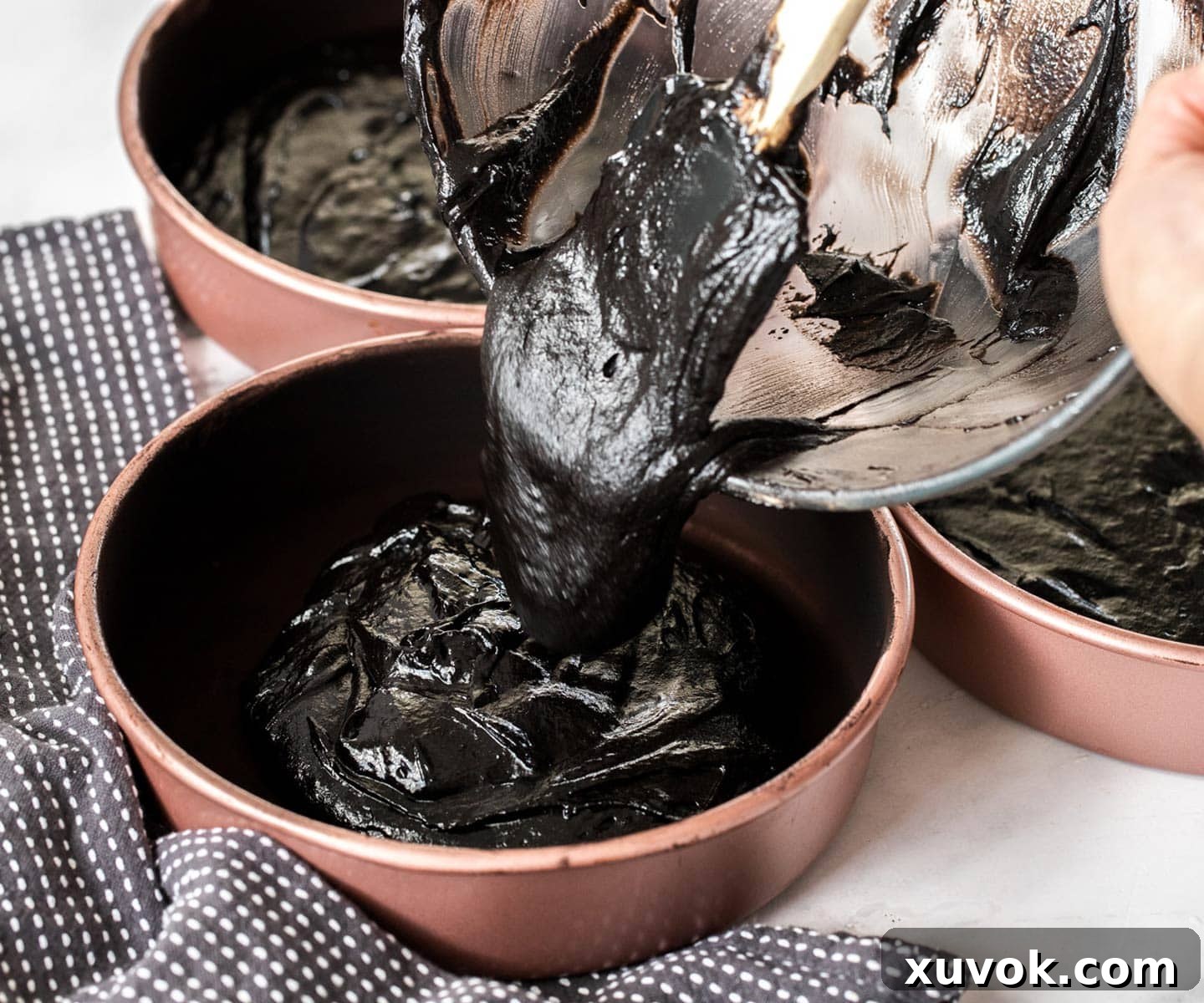 The black velvet cake batter being poured into three separate cake pans, ready for baking.
