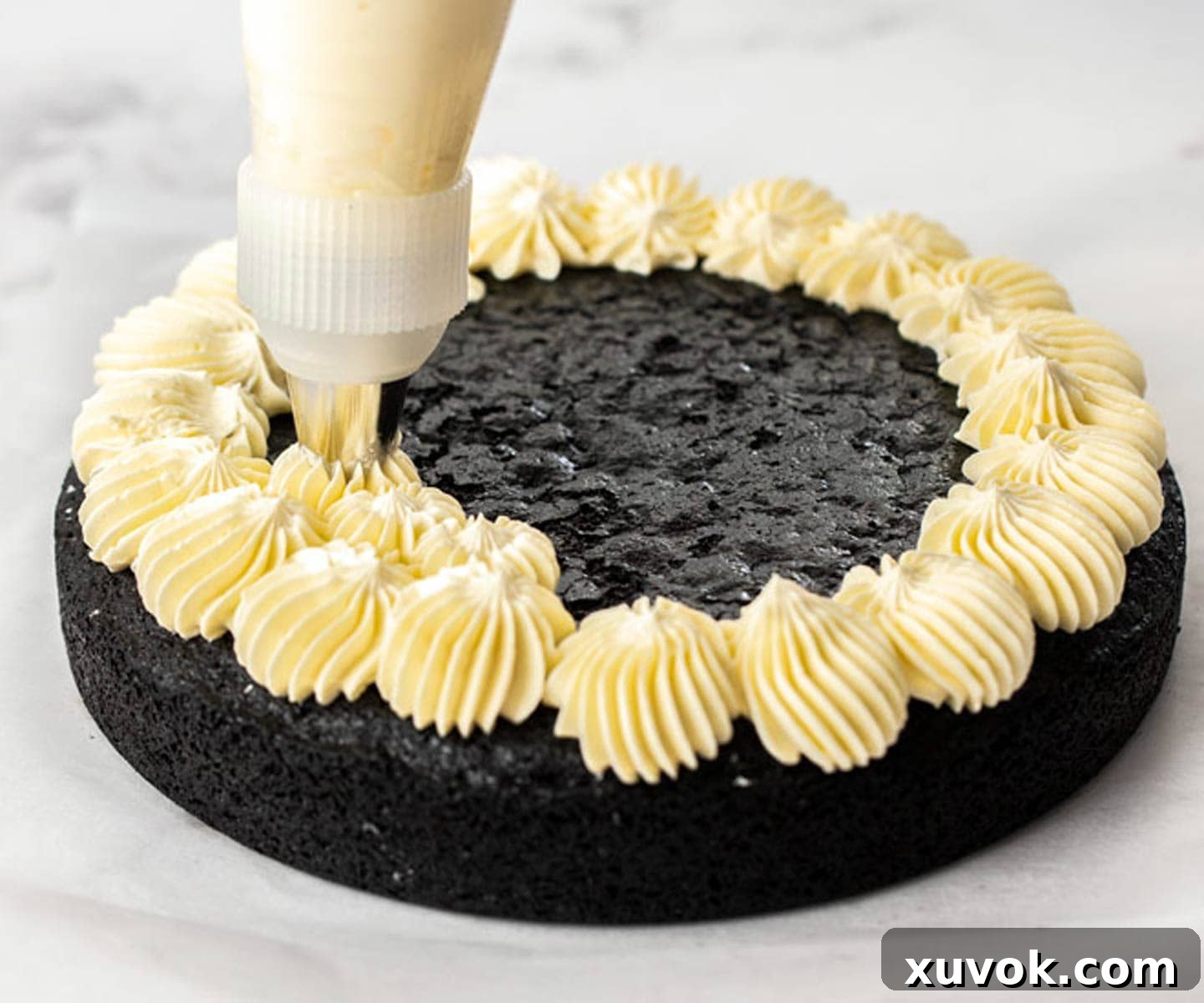 Piping frosting onto a single, flat layer of black velvet cake before stacking.