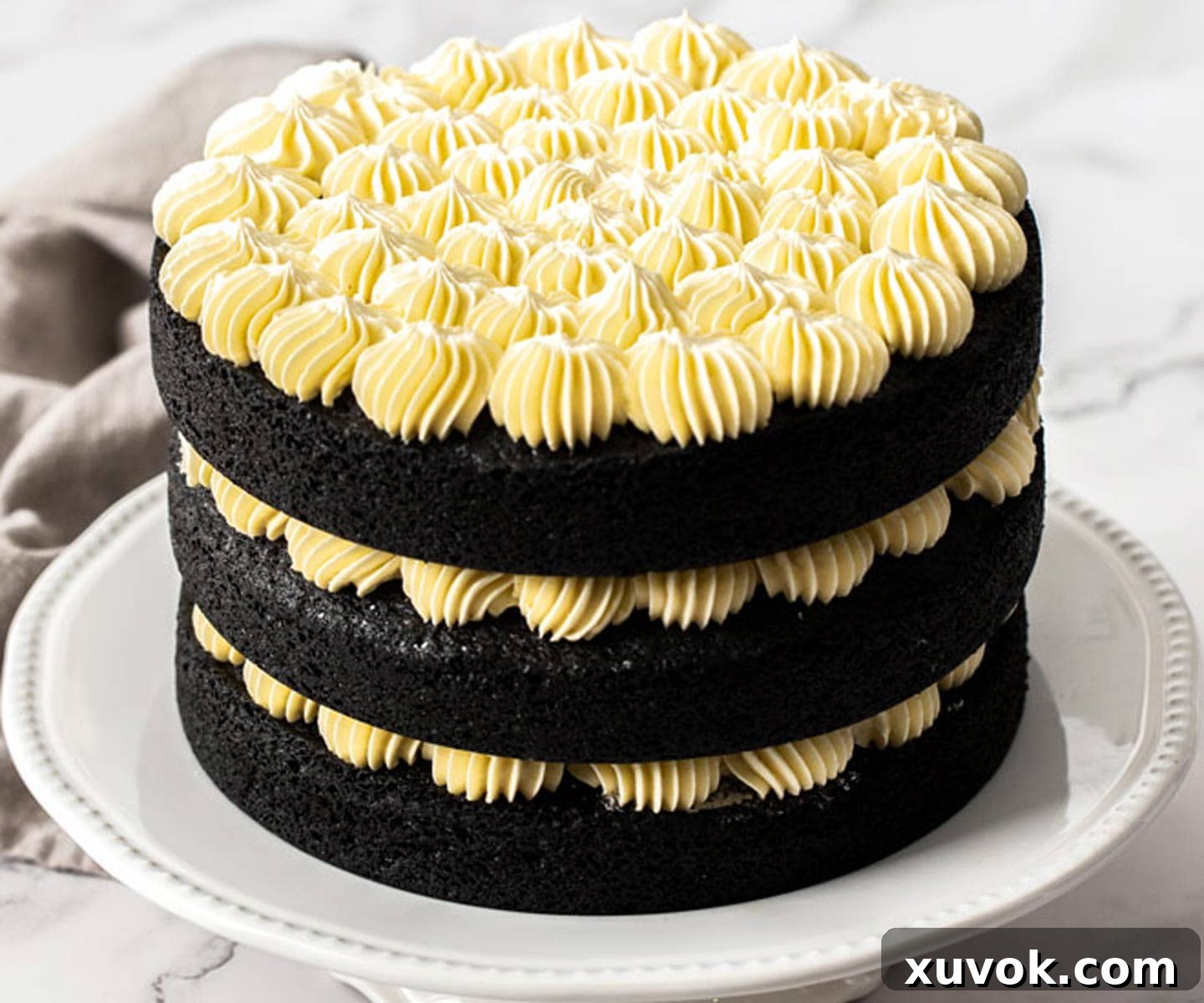 Three layers of black velvet cake, each expertly frosted, are stacked and ready for final decoration with fruit.