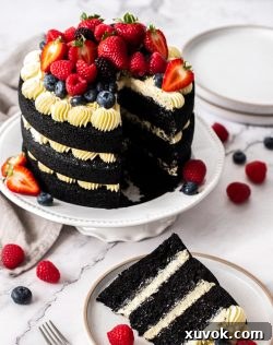 A slice of black velvet cake on a stand with berries