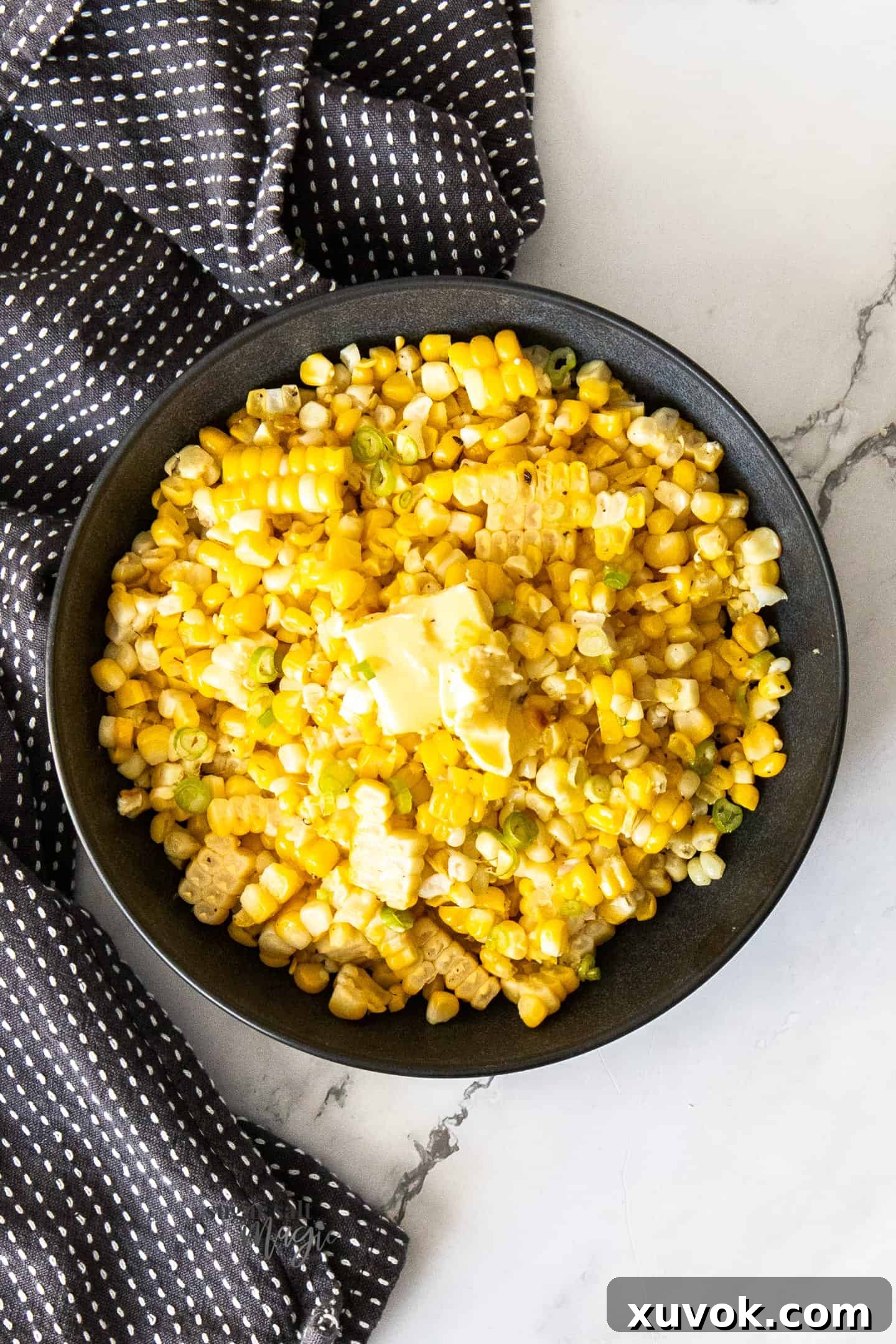 A black ceramic bowl filled with bright yellow cooked corn kernels, glistening with butter.