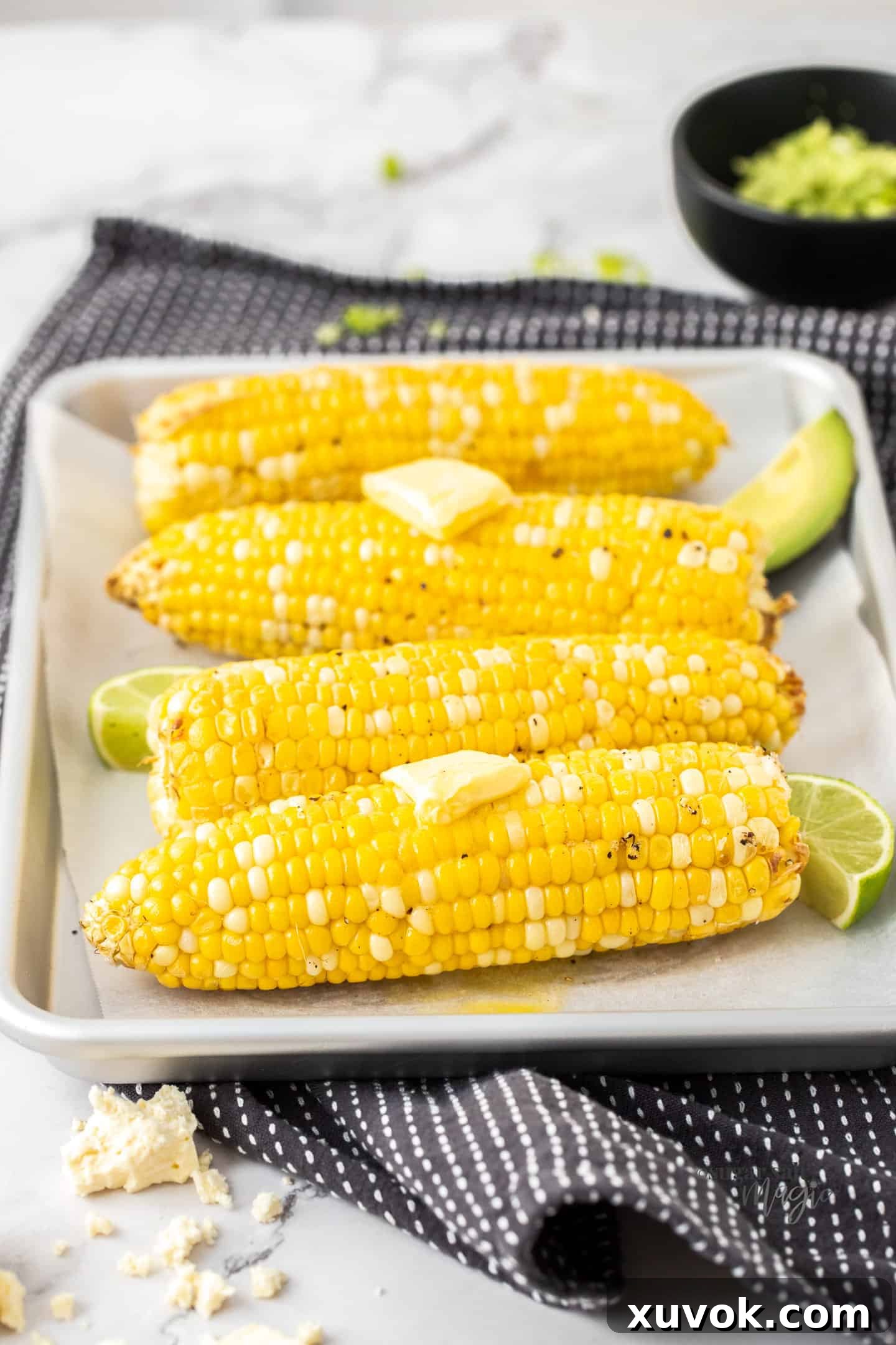 Four air-fried corn cobs arranged on a silver baking tray, each topped with a melting pat of butter, showcasing their tender and golden appearance.