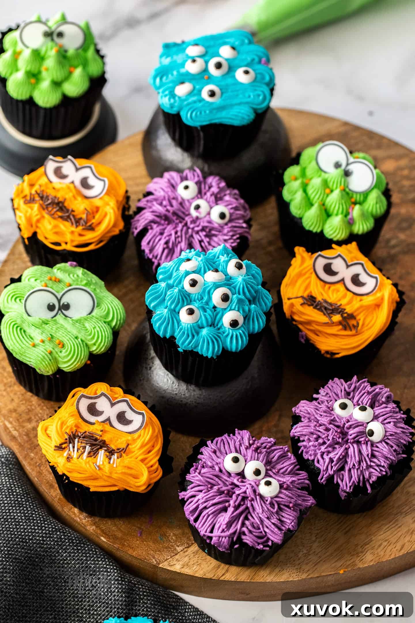 11 colourful cupcakes with candy eyes on a wooden platter. These adorable monster cupcakes are perfect Halloween treats or for birthday parties. Moist and tender dark chocolate cupcakes, topped with a fun, colourful frosting and beady little eyes.