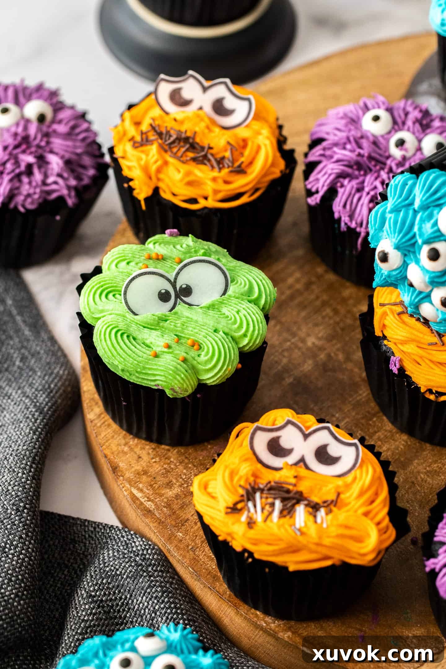 A variety of coloured cupcakes on a wooden platter with candy eyes. These adorable monster cupcakes are perfect Halloween treats or for birthday parties. Moist and tender dark chocolate cupcakes, topped with a fun, colourful frosting and beady little eyes.