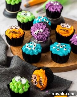 12 colourful cupcakes with candy eyes on a wooden platter.