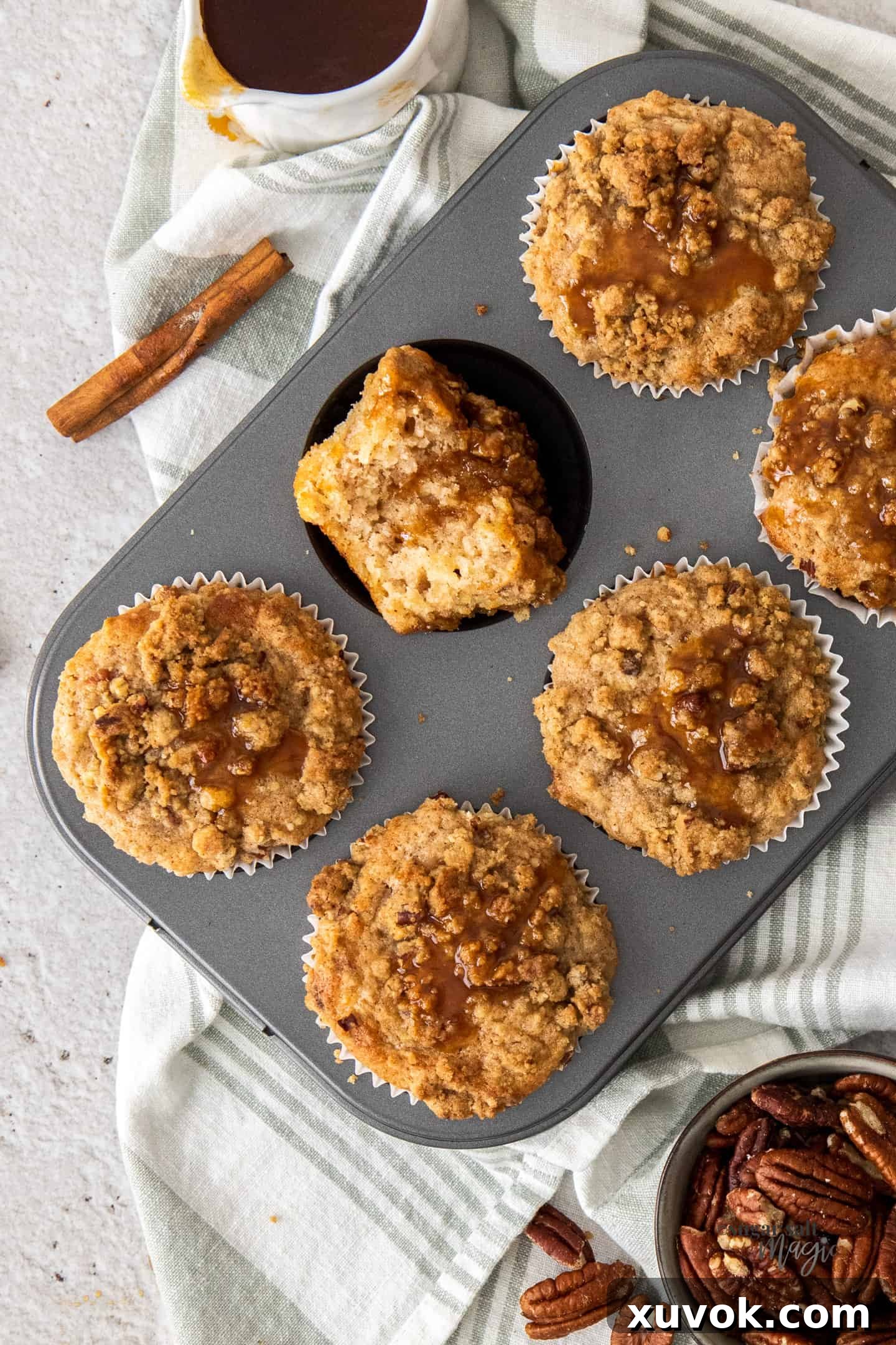 A muffin tin with 6 crumble-topped muffins in it, drizzled with caramel sauce.