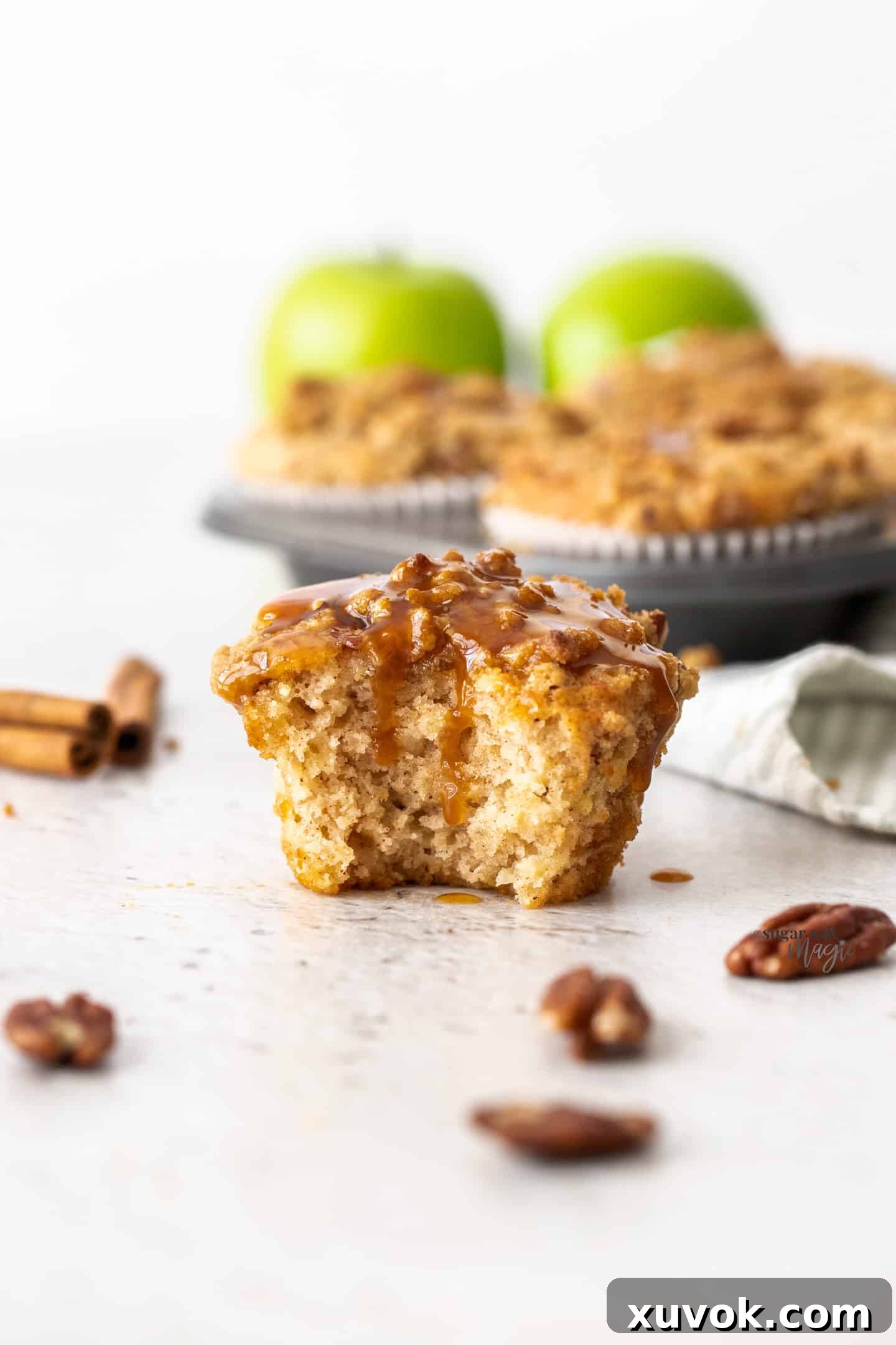 A muffin that's been broken open showing the fluffy, apple-studded inside with streusel on top.