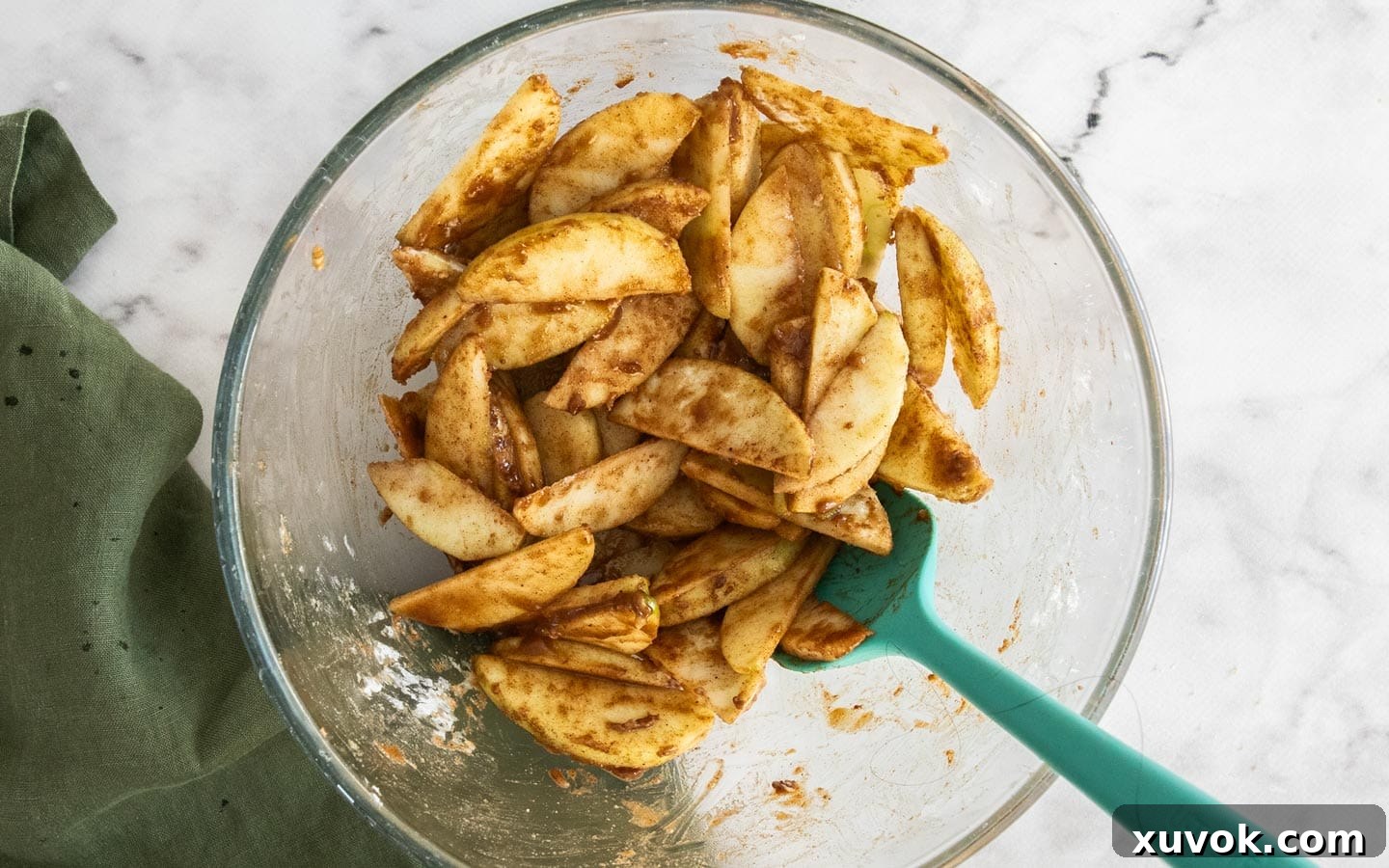 Apple slices being mixed with brown sugar, cinnamon, nutmeg, and flour in a bowl.