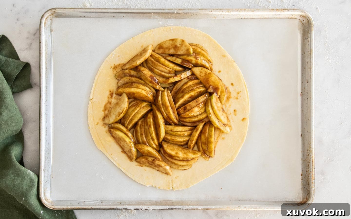 The pastry dough gracefully topped with arranged apple slices, maintaining a clear border.