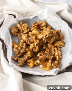 A batch of walnut praline on a sheet of baking paper on a dark tray.