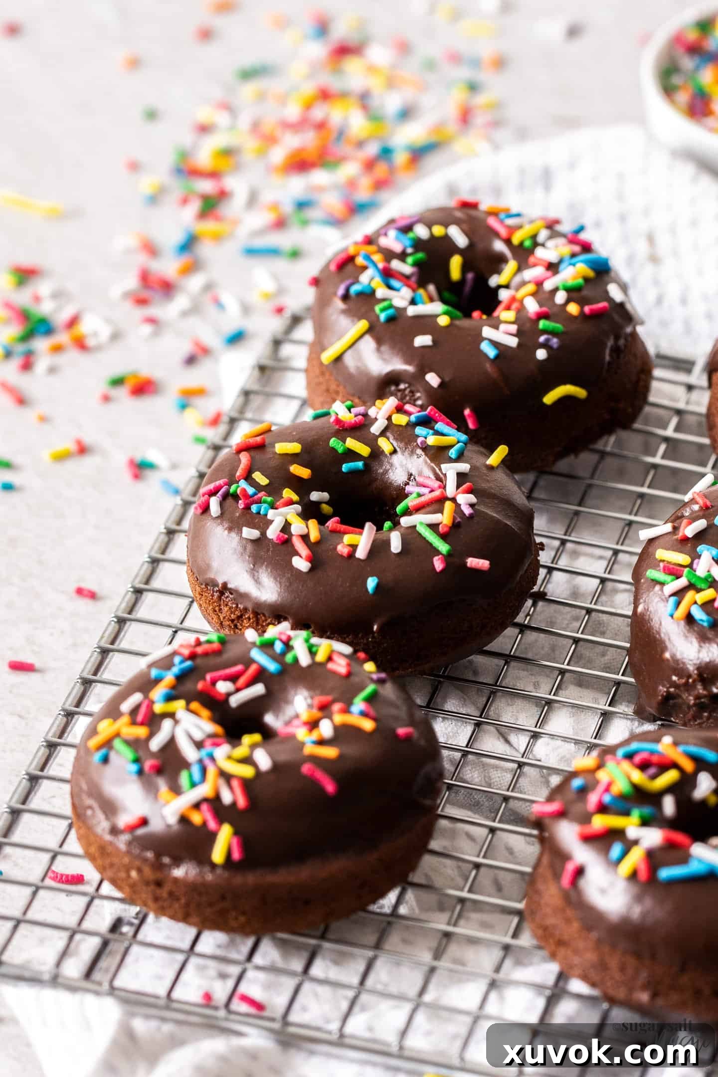 Three delicious chocolate cake donuts covered in colorful sprinkles resting on a wire rack, freshly baked and ready to be devoured.