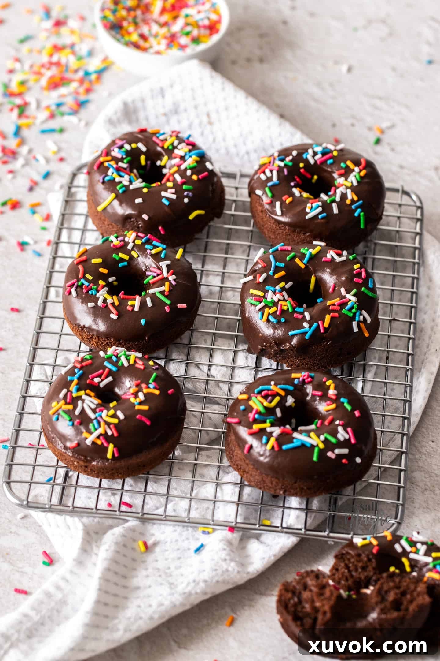 Six perfectly arranged chocolate sprinkle donuts on a wire rack, with a bowl of vibrant sprinkles in the background, ready to be enjoyed.