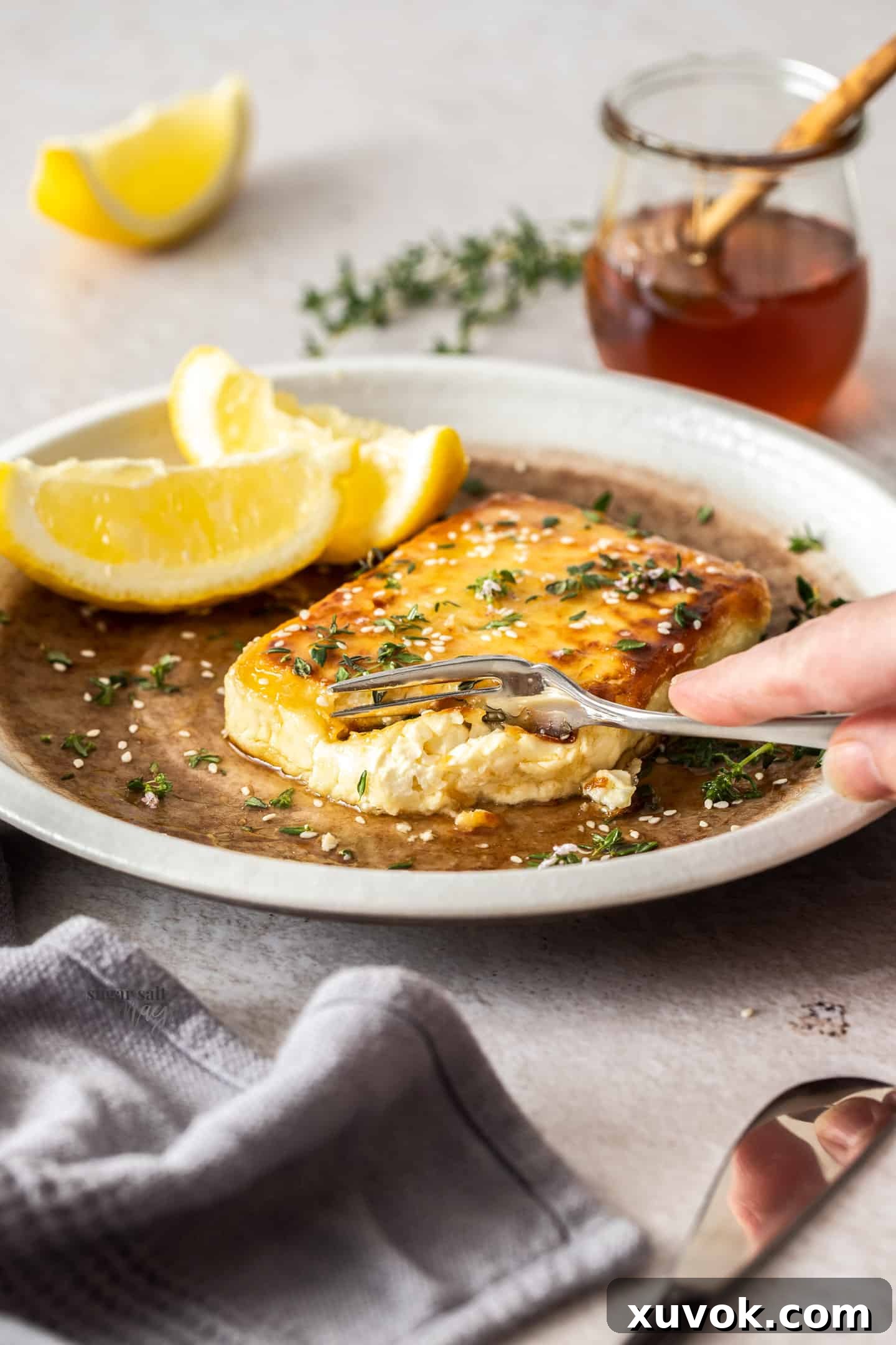 A fork cutting into a perfectly pan-fried square of feta saganaki, showing its crispy golden crust and soft, creamy interior.