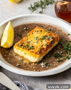 A slice of fried feta on a plate with a lemon wedge on the side, ready to be enjoyed.