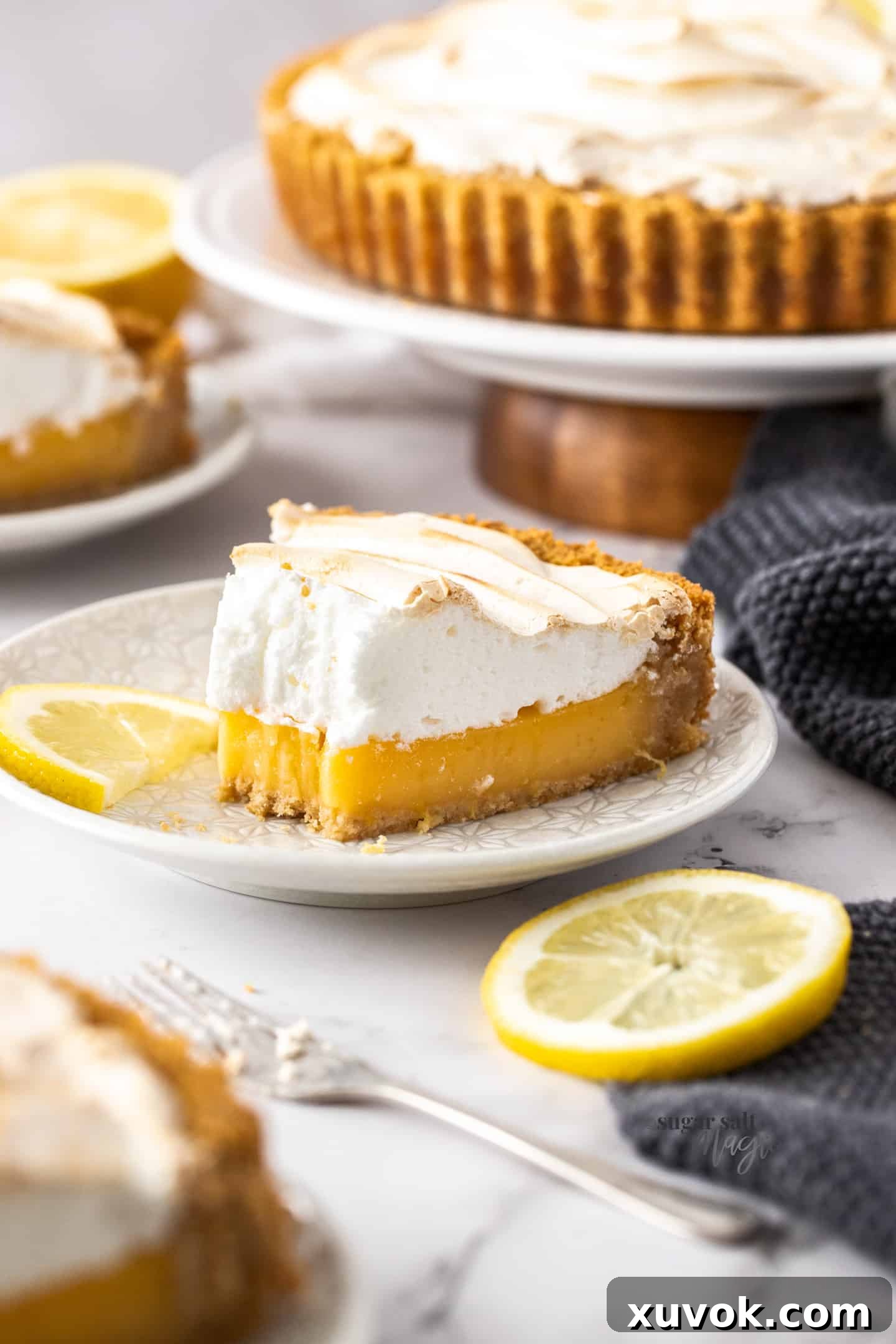 A beautiful slice of lemon meringue pie on a white plate, with a forkful already taken out, highlighting the fluffy meringue and vibrant lemon filling.