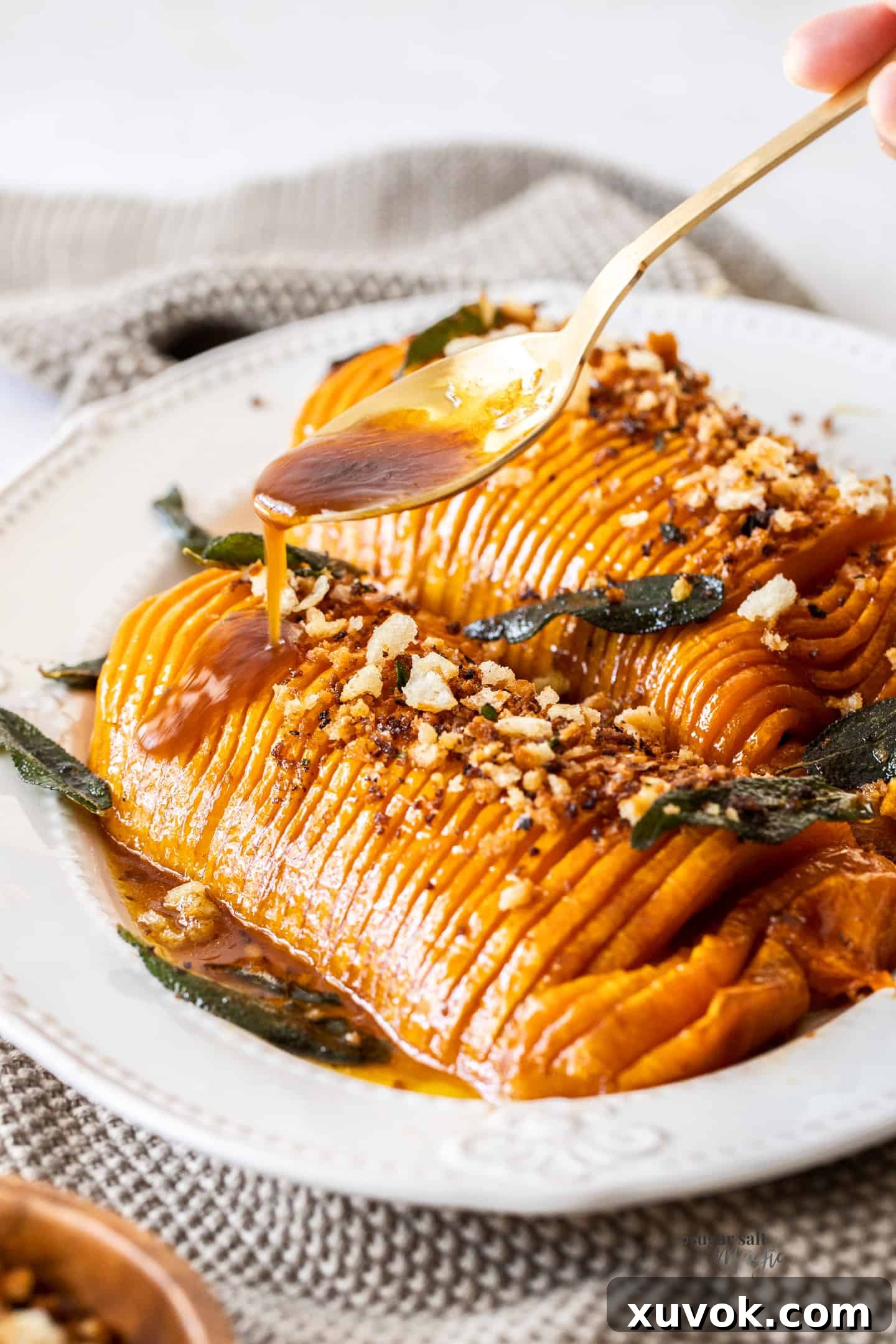 A close-up shot of golden-brown pan juices being drizzled over roasted hasselback butternut squash on a white platter, enhancing its glossy finish.