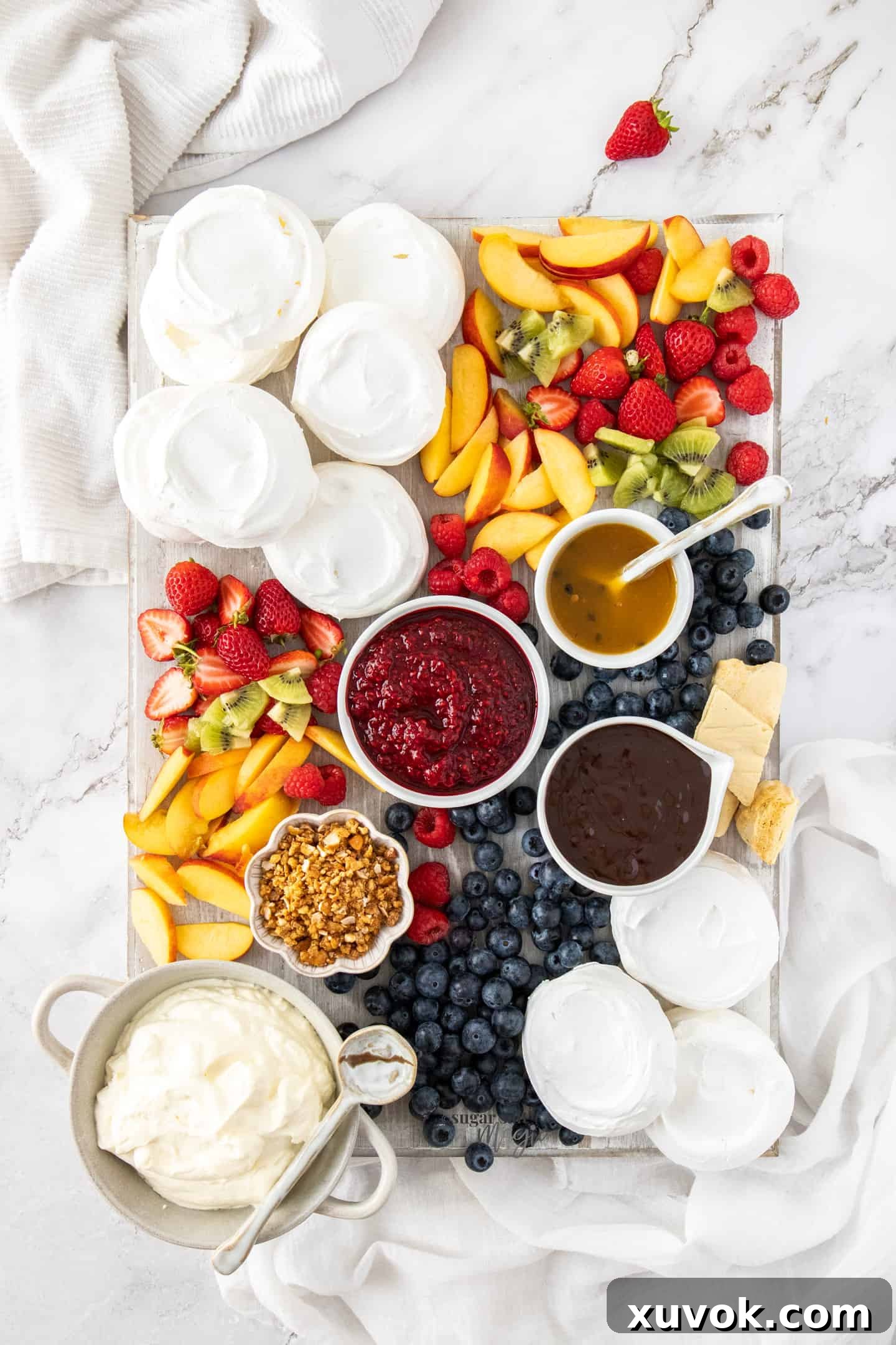 Top down view of a board filled with crispy meringues, colorful fresh fruit, and rich sauces, ready for a dessert buffet.