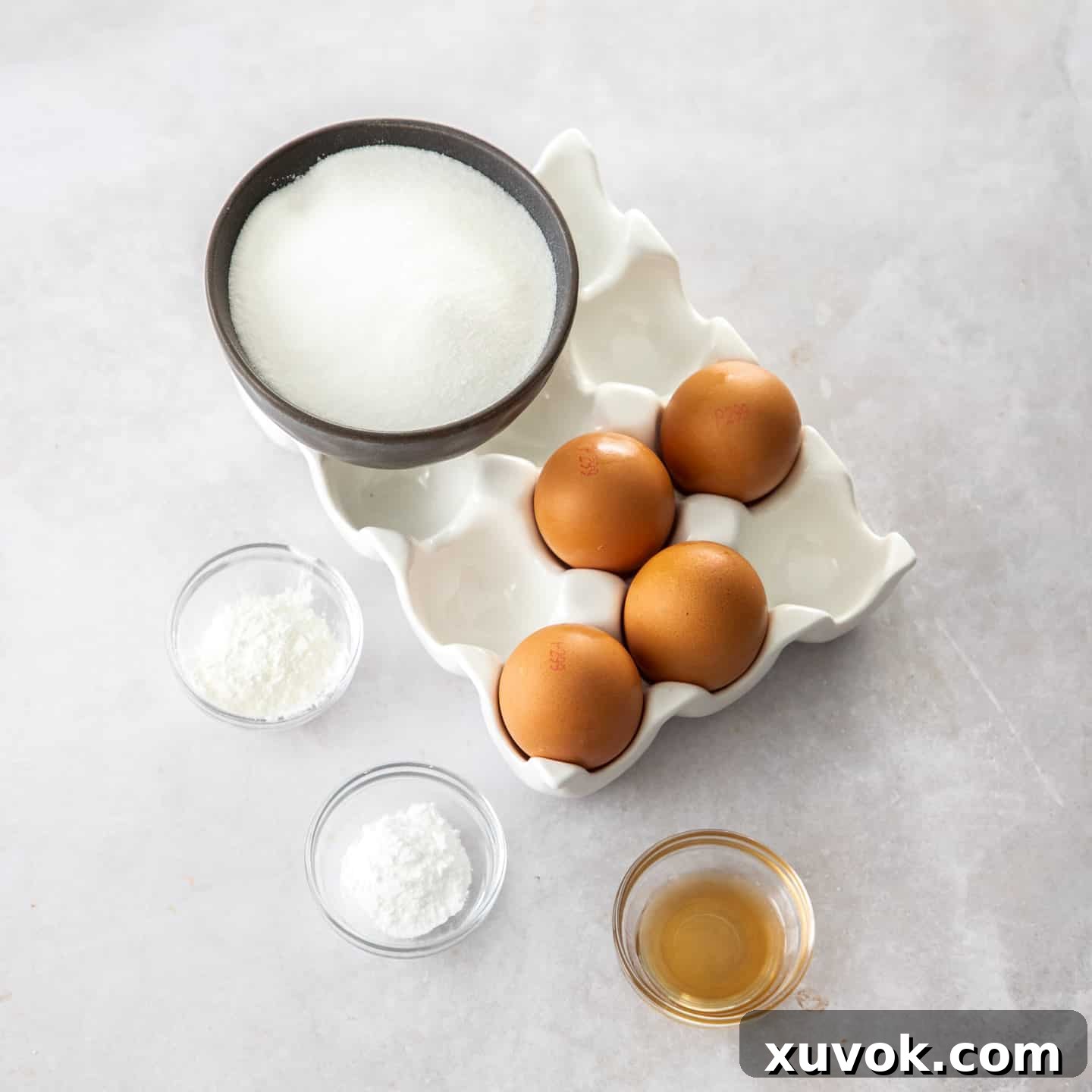 Ingredients for pavlova, including eggs, sugar, and cornflour, neatly arranged on a grey benchtop.