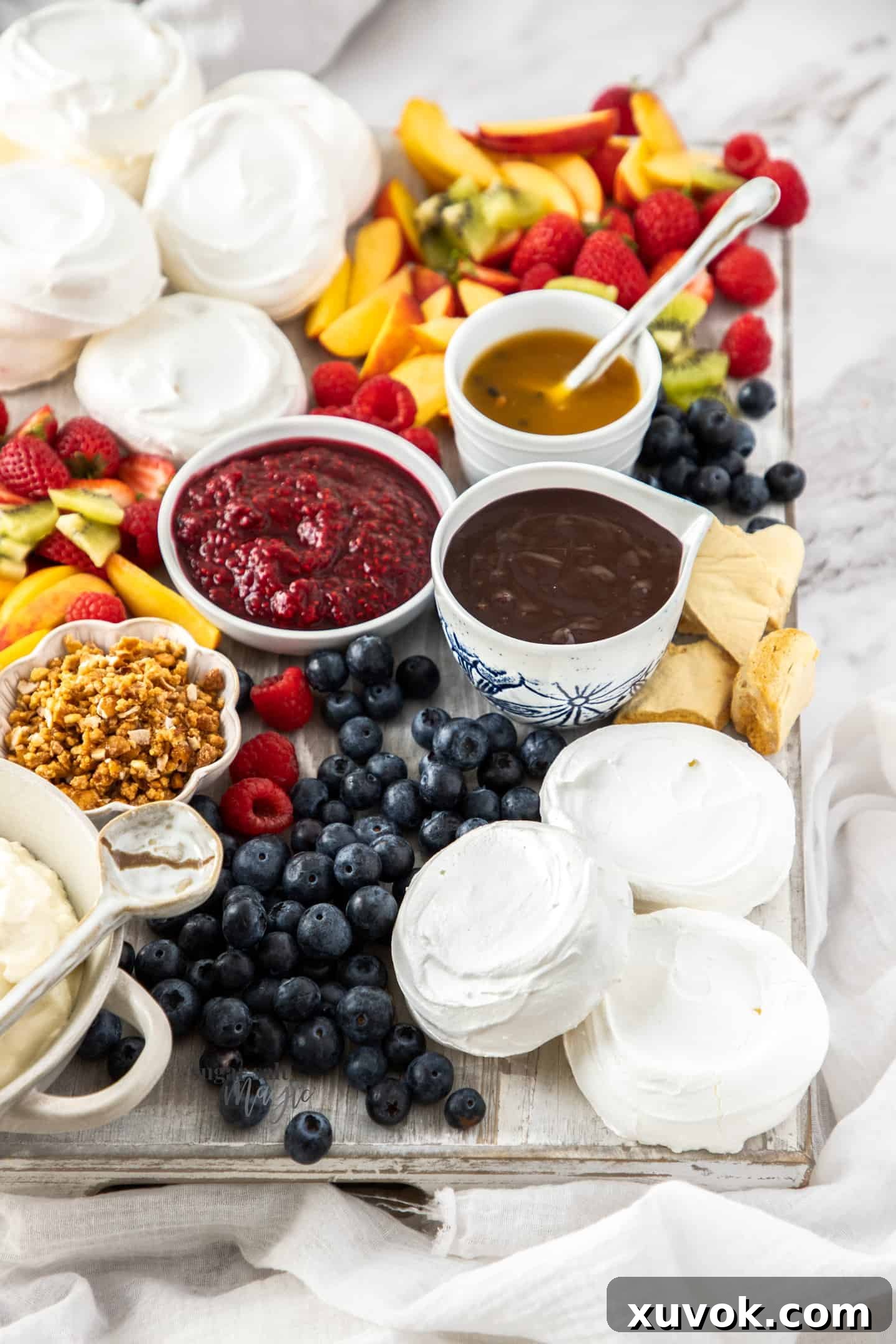 A beautifully arranged grazing board brimming with individual meringue shells, various sweet sauces, and an abundance of colorful fresh fruits.