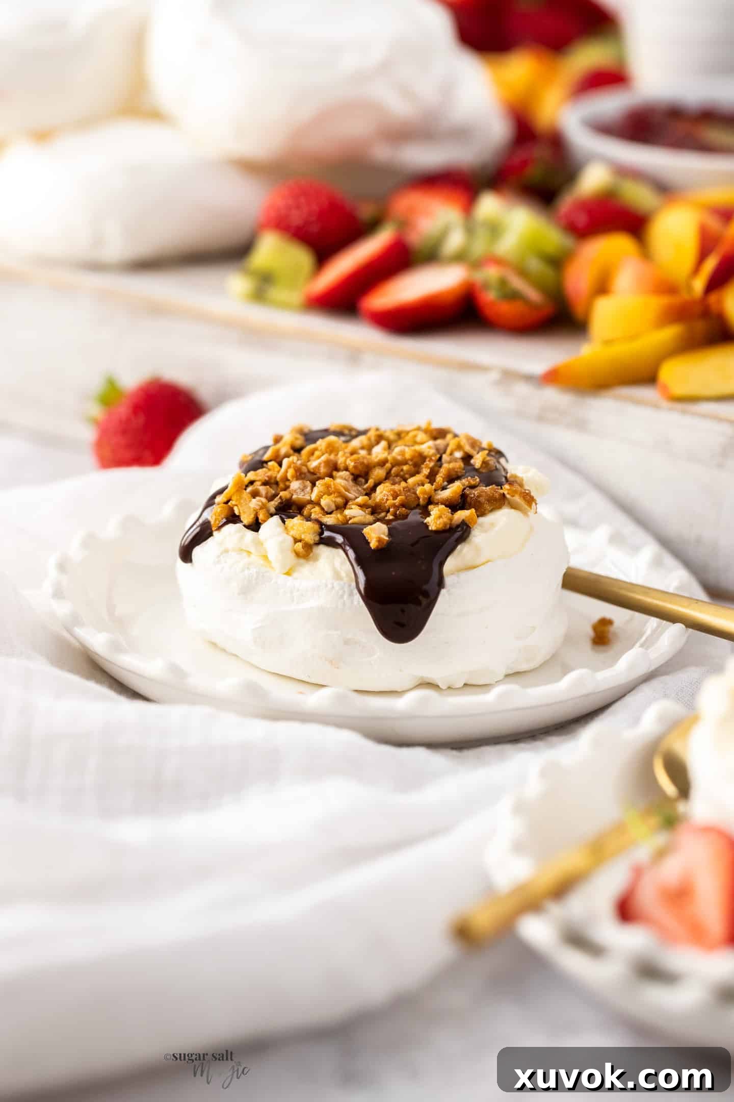A close-up of a mini pavlova generously topped with rich chocolate ganache, placed on a dainty dessert plate.