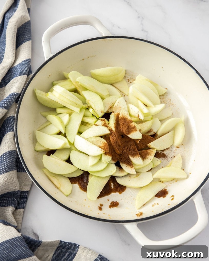 A white pan filled with sliced apples, cinnamon, sugar and butter.