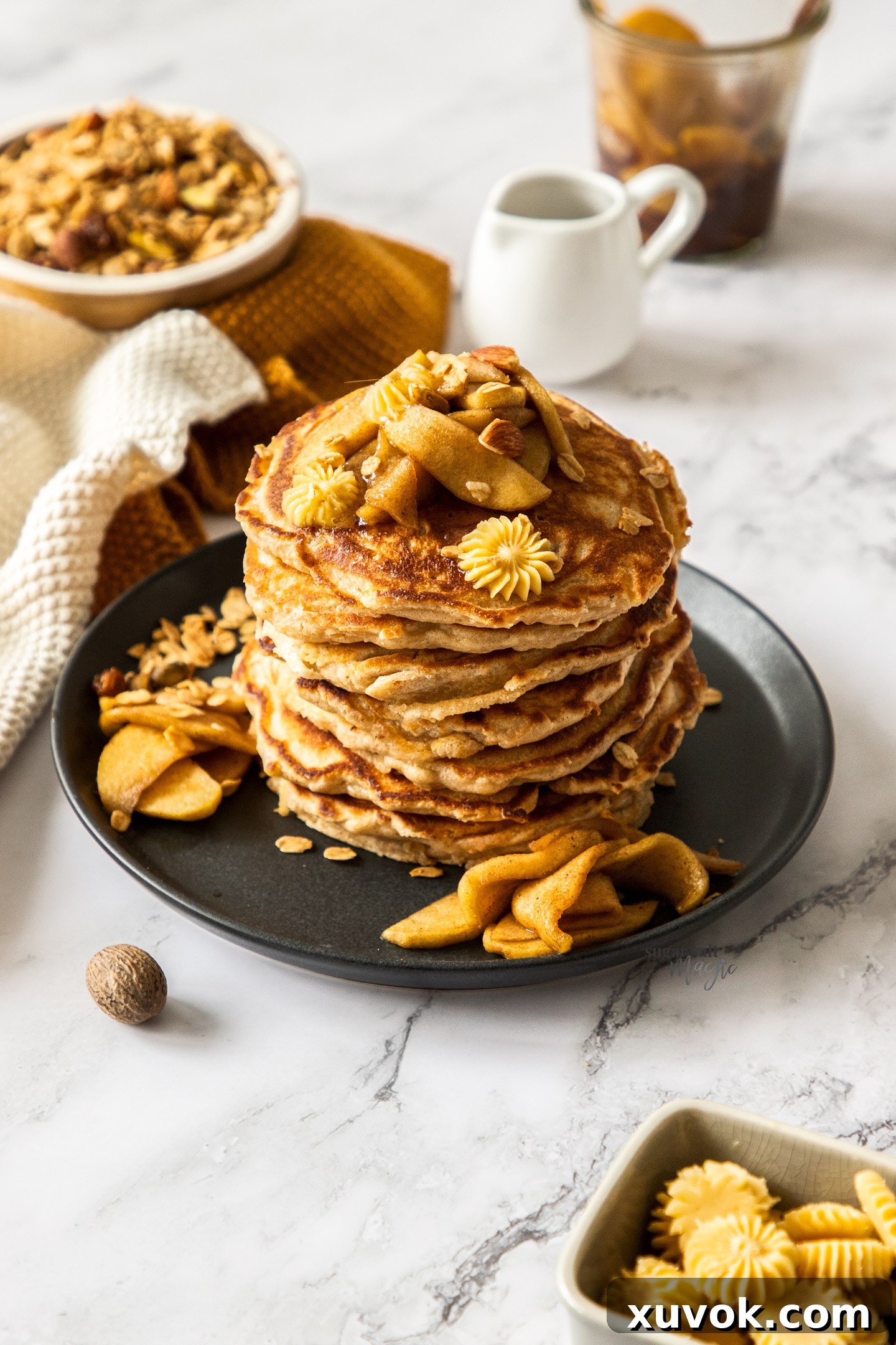 A stack of pancakes topped with apples and butter.