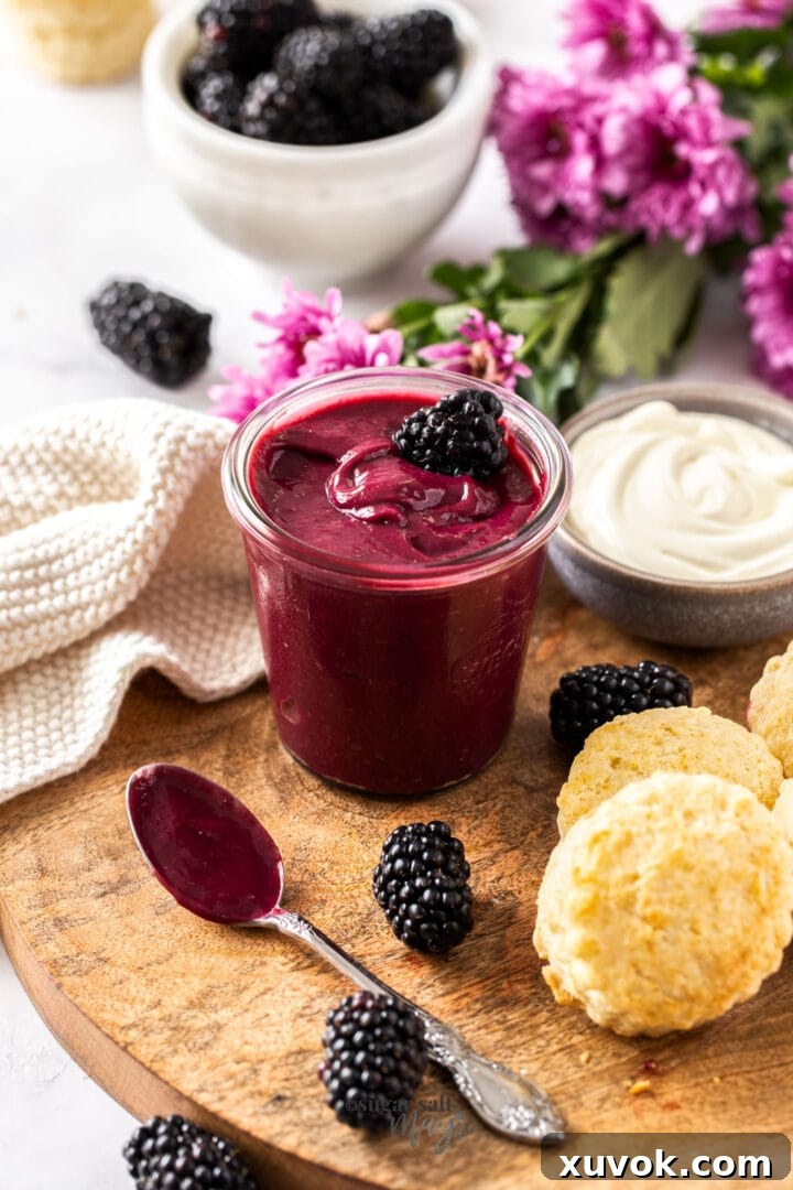 A glass jar filled with luscious homemade blackberry curd, surrounded by fresh blackberries and golden scones, highlighting its rich texture and versatility for various culinary delights.