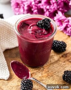 A glass jar filled with luscious blackberry curd, surrounded by fresh blackberries, illustrating the rich, vibrant color and smooth texture of the homemade spread.