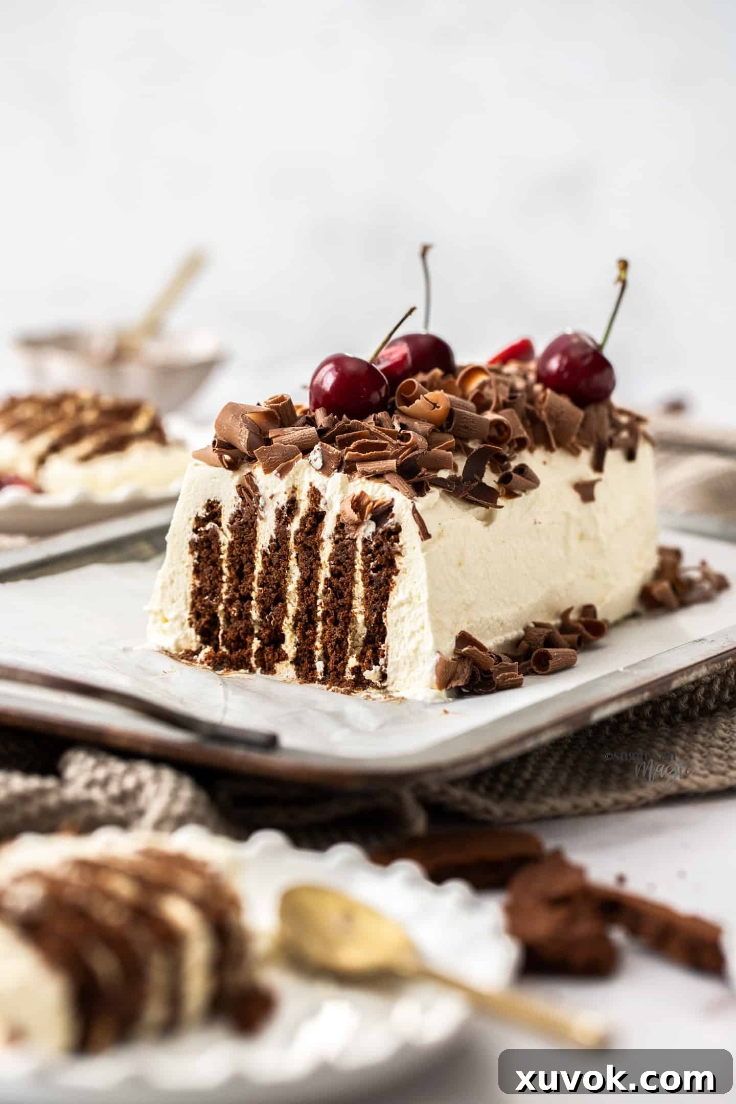 A no-bake chocolate ripple cake covered generously with vanilla whipped cream, garnished with chocolate curls and fresh cherries, set against a bright background, showcasing its delicious appeal.