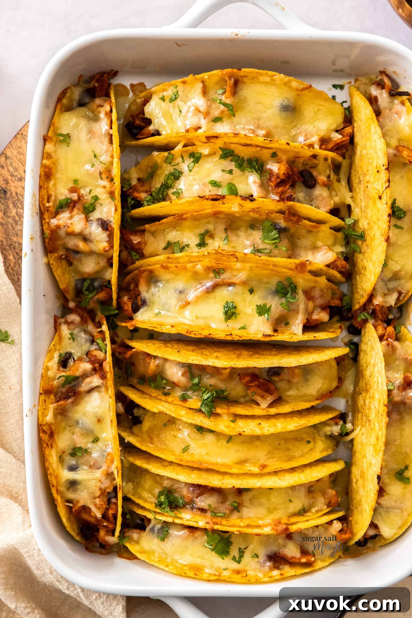 Crispy baked chicken tacos with melted cheese, arranged in a baking dish, ready for toppings.
