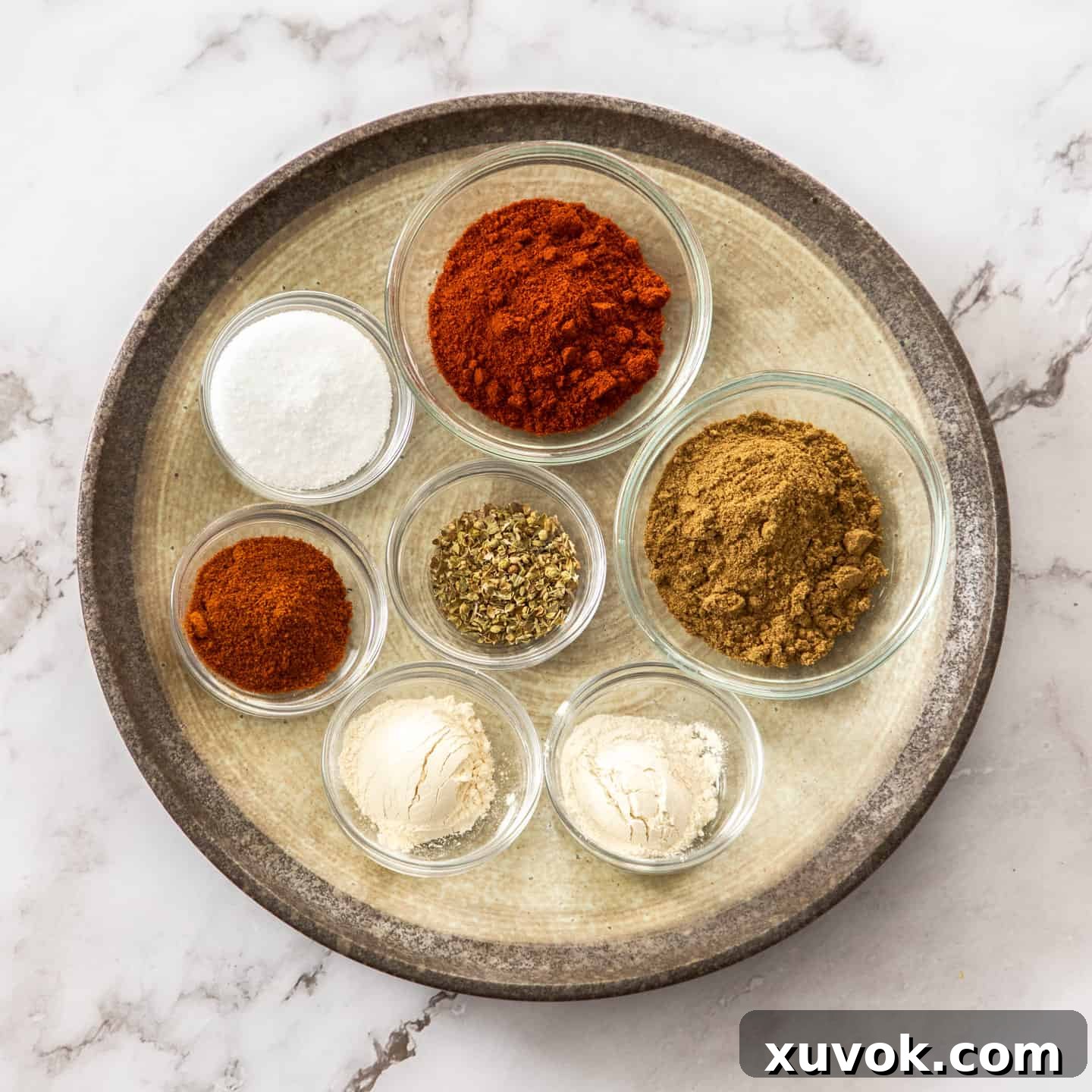 A selection of individual spices laid out on a round plate, including cumin, paprika, chili powder, and oregano, ready for making homemade taco seasoning.