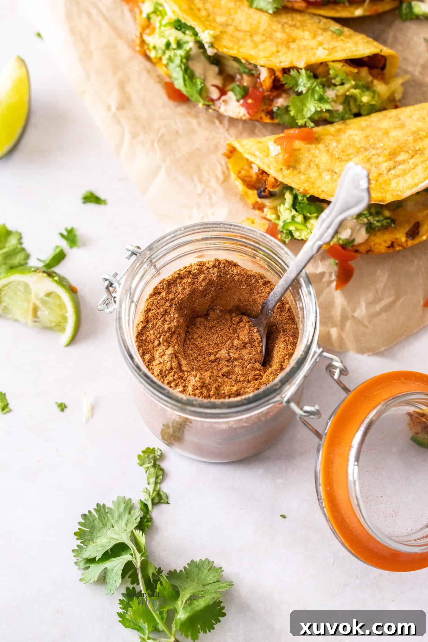 A small jar of homemade taco seasoning placed next to a plate of delicious, freshly prepared tacos, ready for a meal.