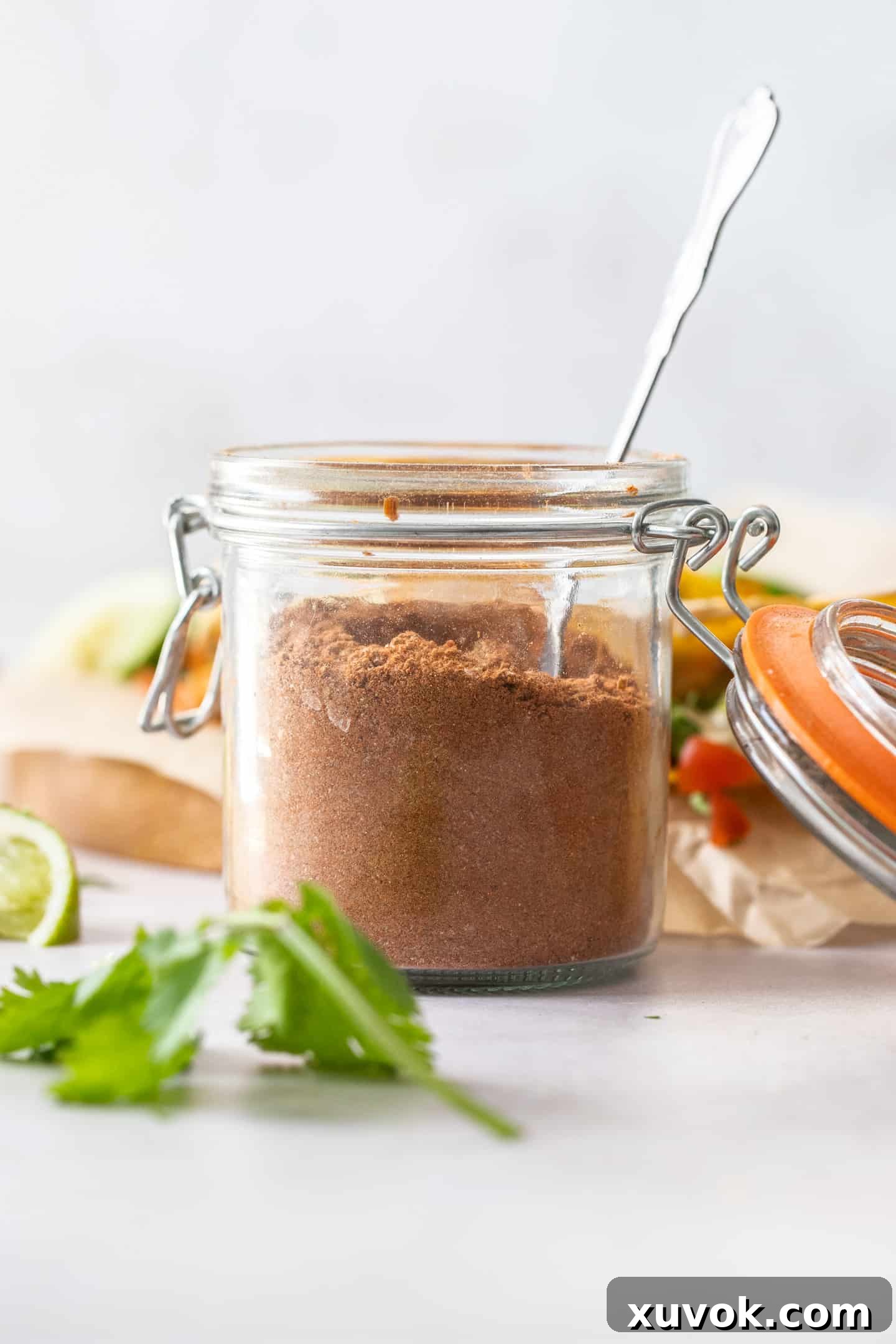 A small jar filled with homemade taco seasoning, with a spoon dipping into it, showcasing its rich texture and color.
