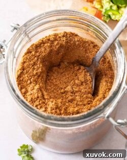 A small jar of homemade taco seasoning with a spoon sticking out, highlighting its rich texture.
