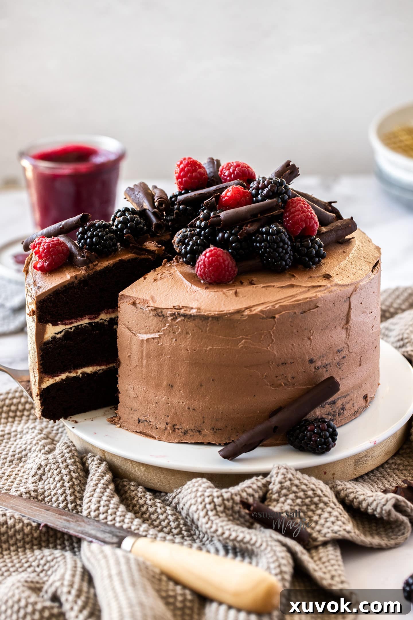 A stunning three-layer chocolate cake generously topped with an assortment of fresh berries and elegant chocolate curls, ready for a special celebration.