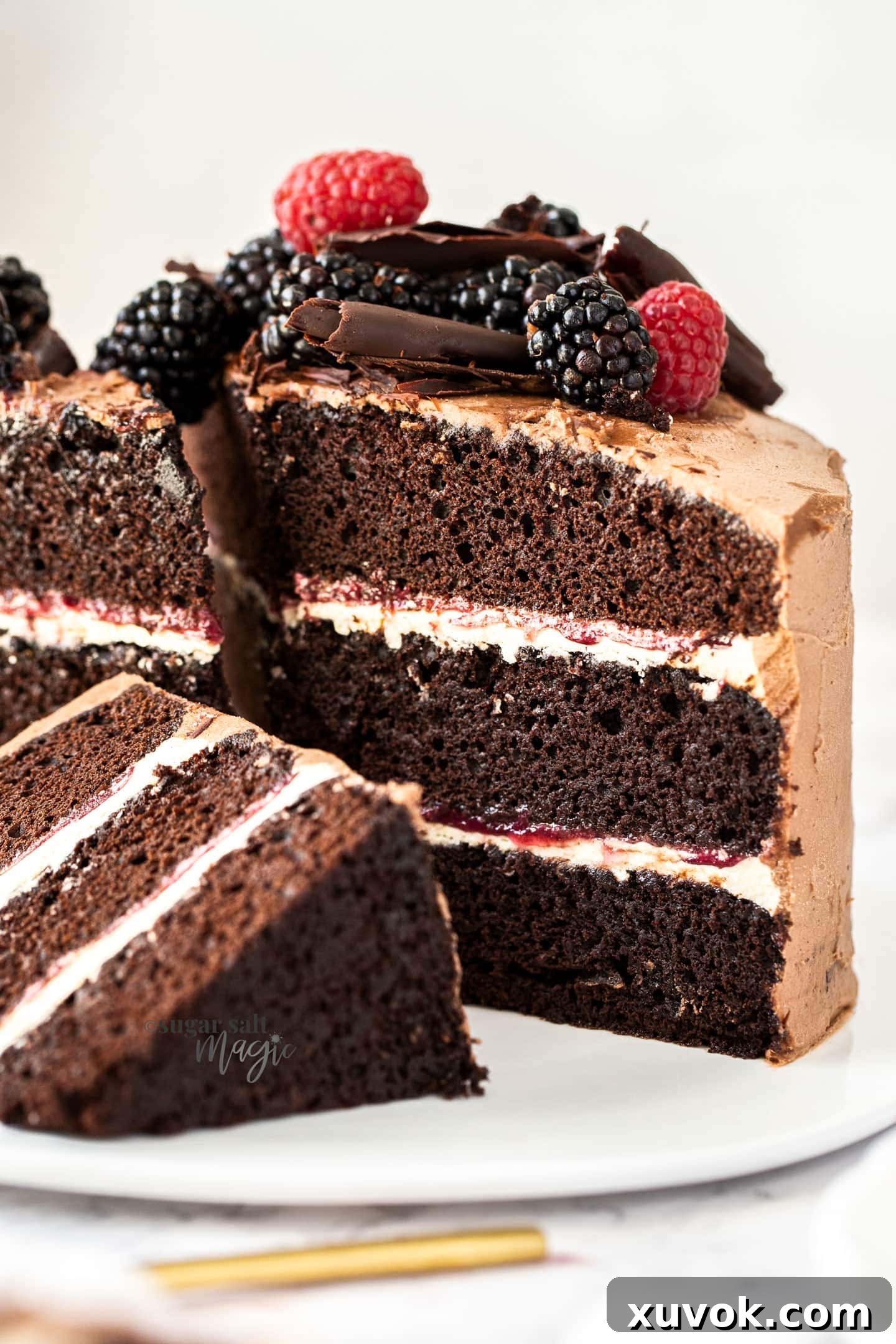 A mouth-watering close-up view of the interior of the three-layer chocolate cake, revealing the moist chocolate layers interspersed with creamy vanilla buttercream and swirls of vibrant blackberry curd.