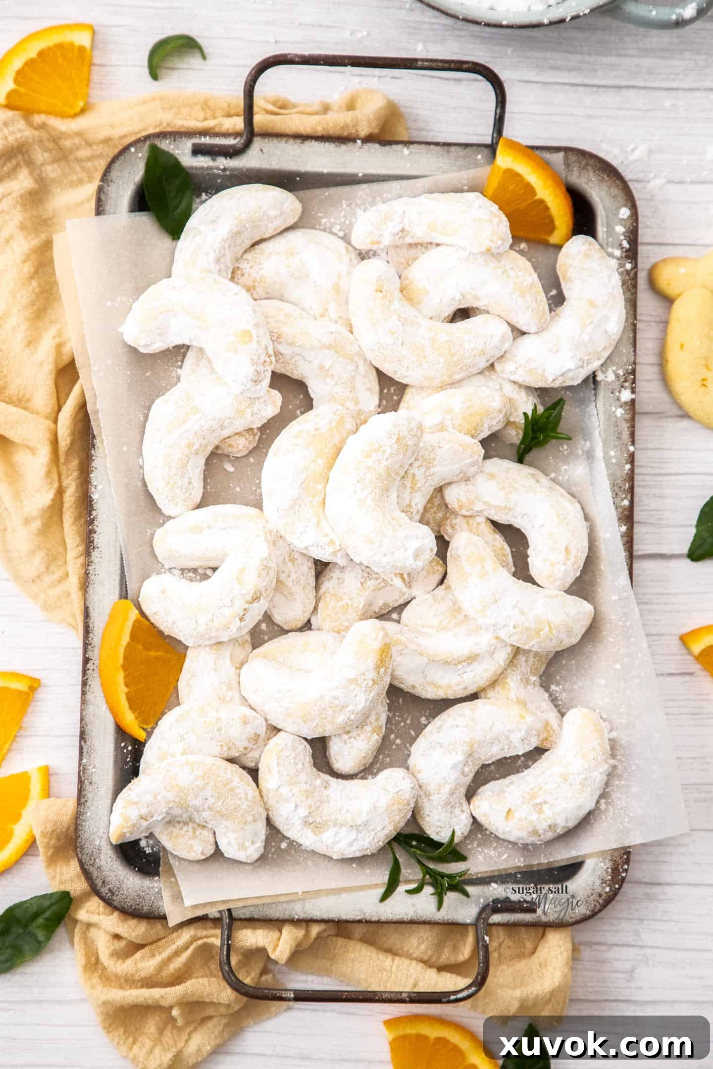 A beautifully arranged batch of golden orange almond crescent cookies on a metal cooling tray, generously dusted with powdered sugar, ready to be enjoyed.