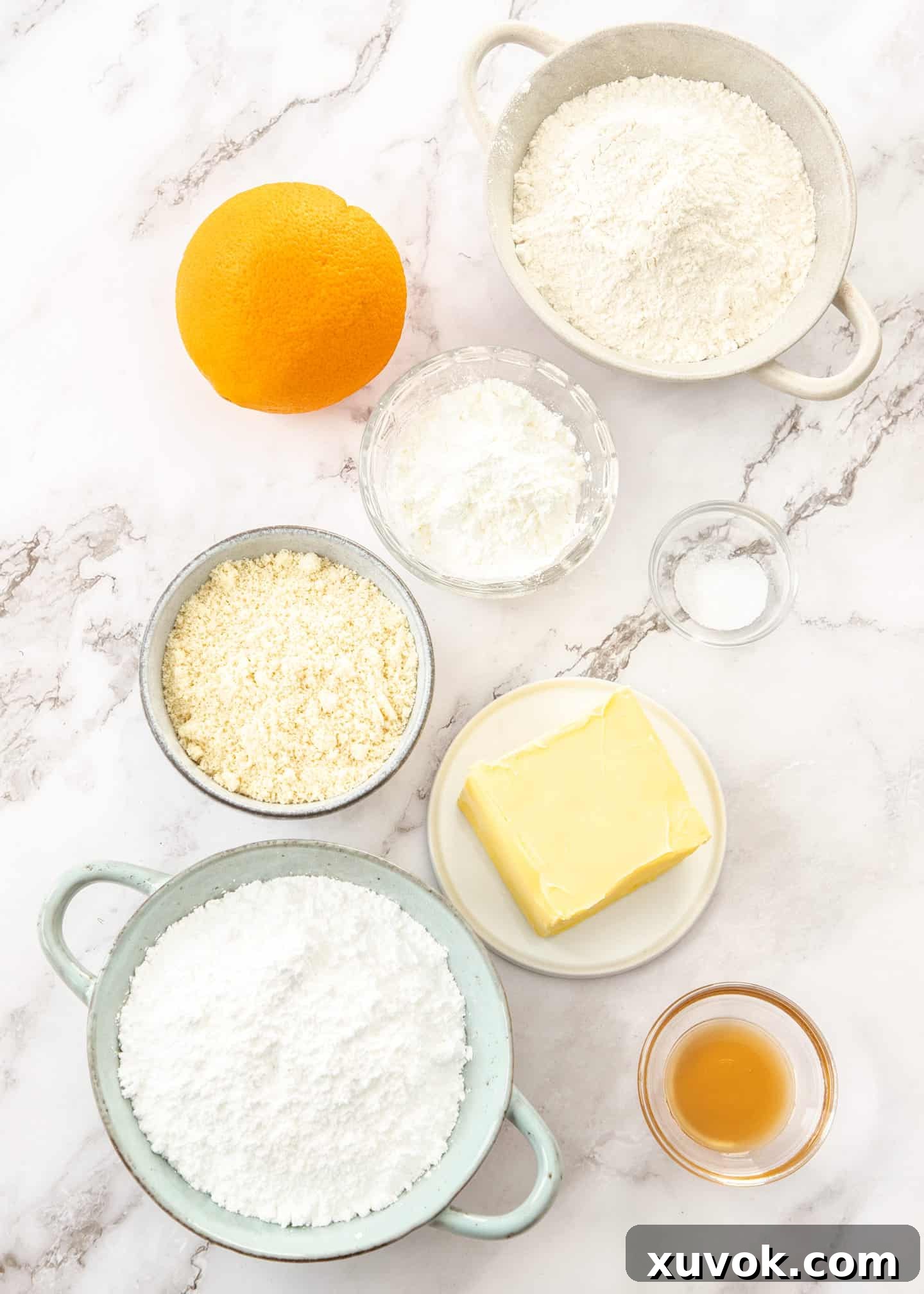 All the necessary ingredients for baking orange almond crescent cookies, neatly arranged on a pristine marble surface, highlighting fresh orange, butter, and flours.
