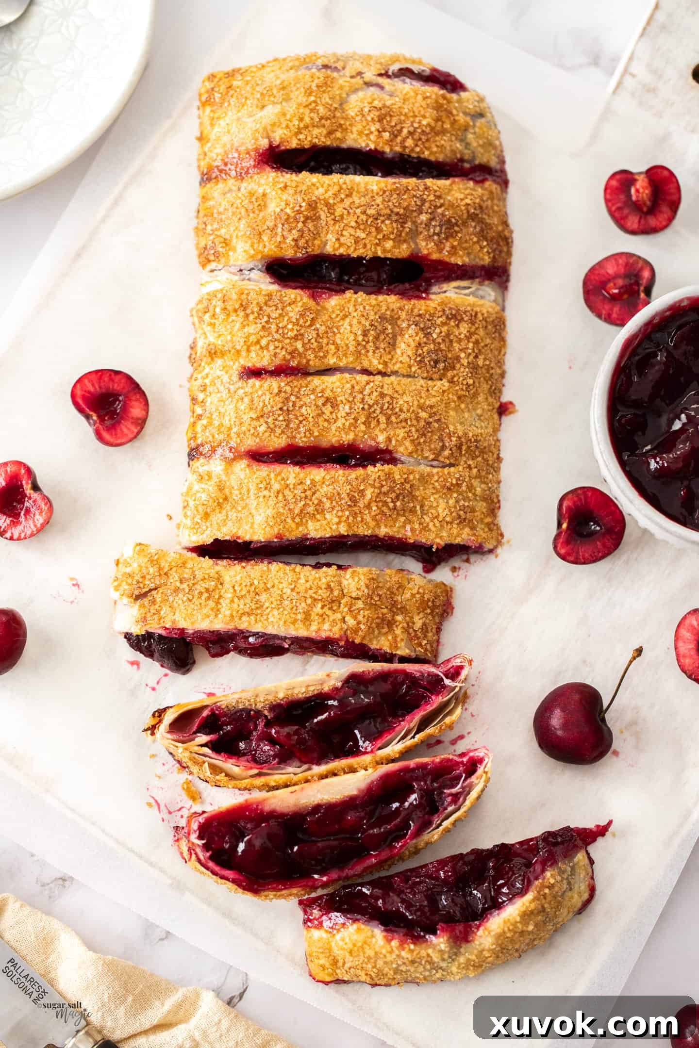 Top down view of cherry strudel with half of it cut, showcasing flaky pastry and vibrant cherry filling.