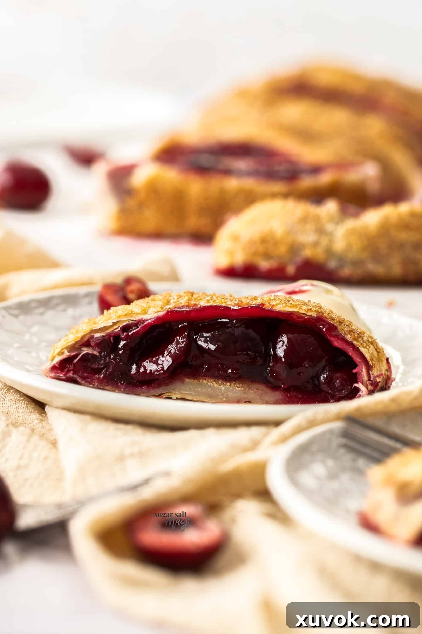 Closeup of a slice of cherry strudel on a small dessert plate, highlighting the flaky pastry and juicy cherry filling.