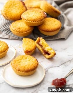 A batch of coconut tartlets with one broken in half to show the jam centre.
