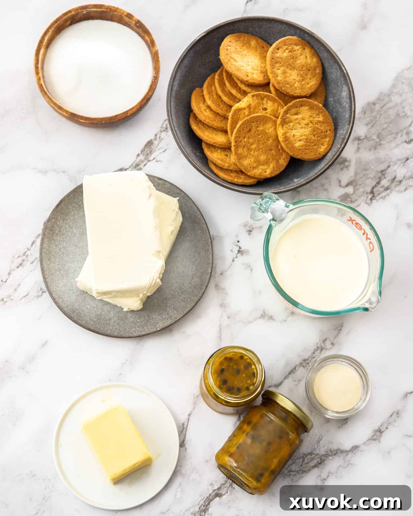 Ingredients for no-bake passionfruit cheesecake laid out on a marble countertop, including cream cheese, butter, passionfruit, and cookies.