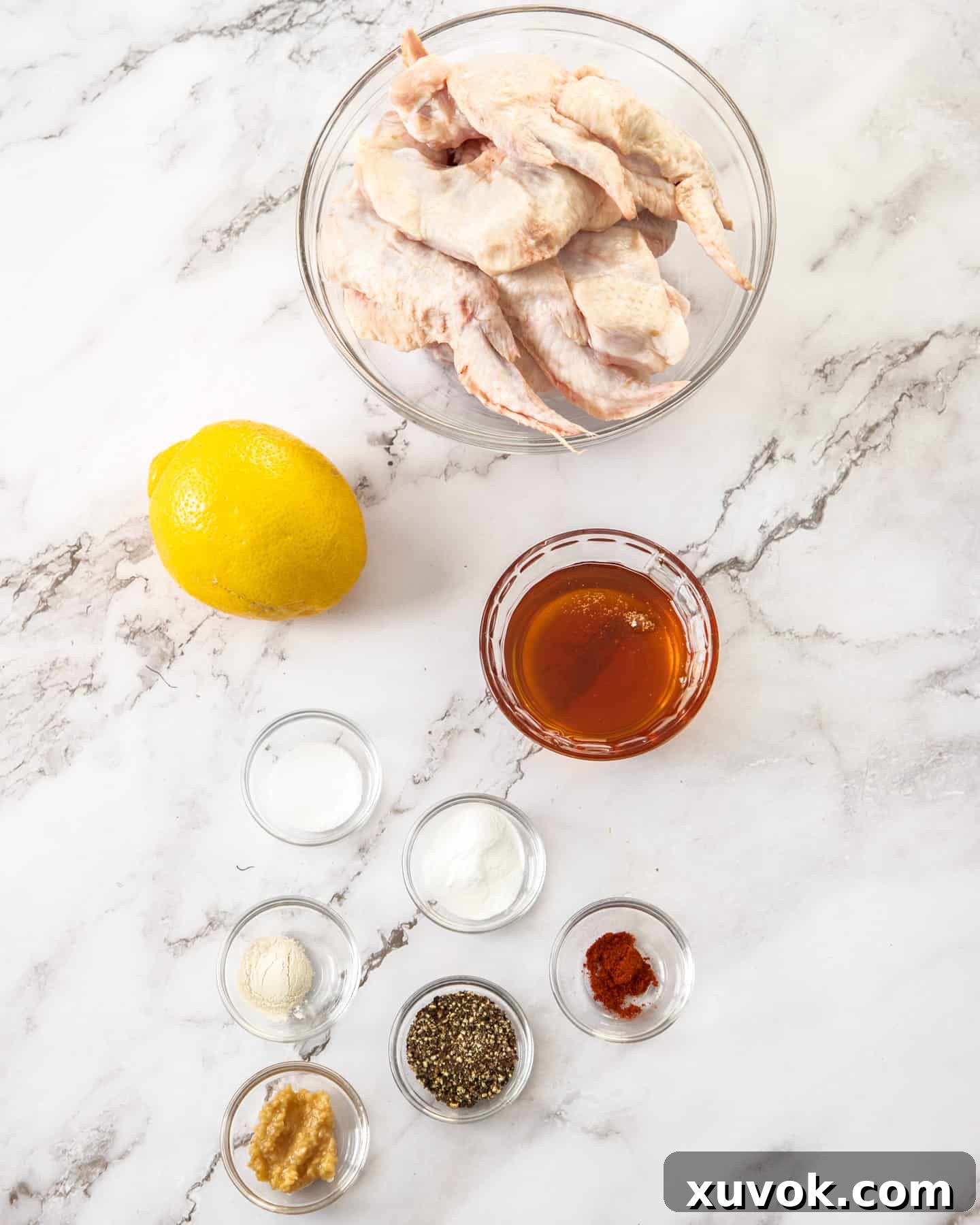 Ingredients for homemade honey lemon pepper chicken wings laid out on a marble countertop, including fresh lemons, honey, pepper, and chicken wings.